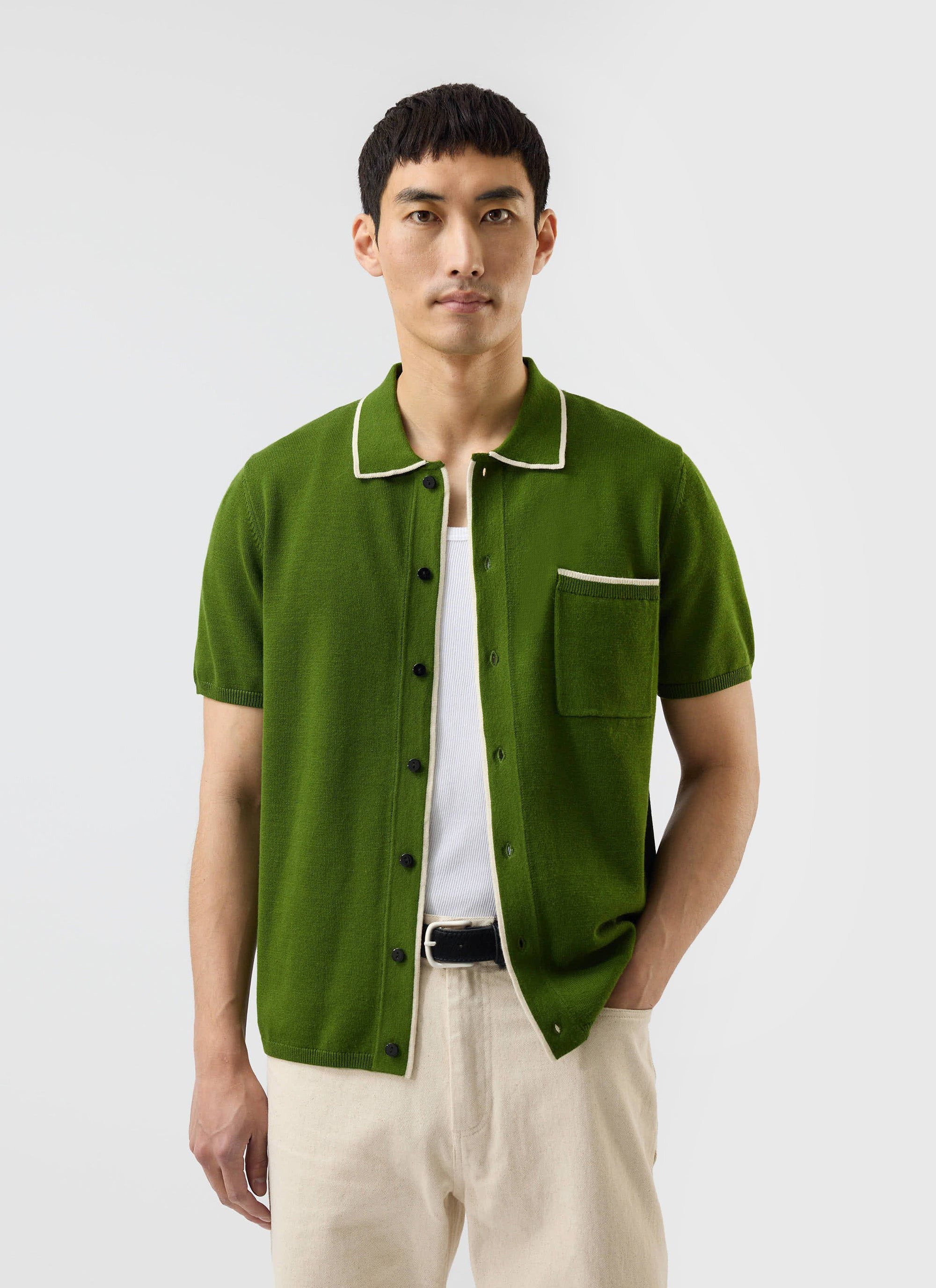 A man models the Percival Contrast Trim Shirt in forest green, a wool-blend knit styled open over a white vest.