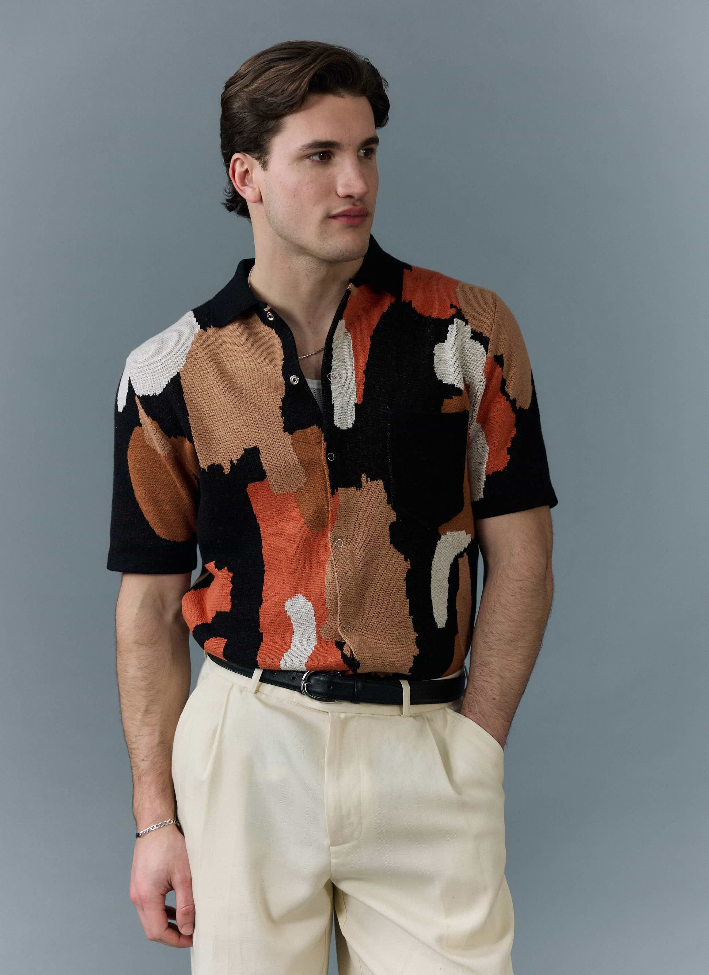 Model wears the Percival Impressionist Jacquard Shirt, a black knitted shirt with an orange, brown and cream pattern.