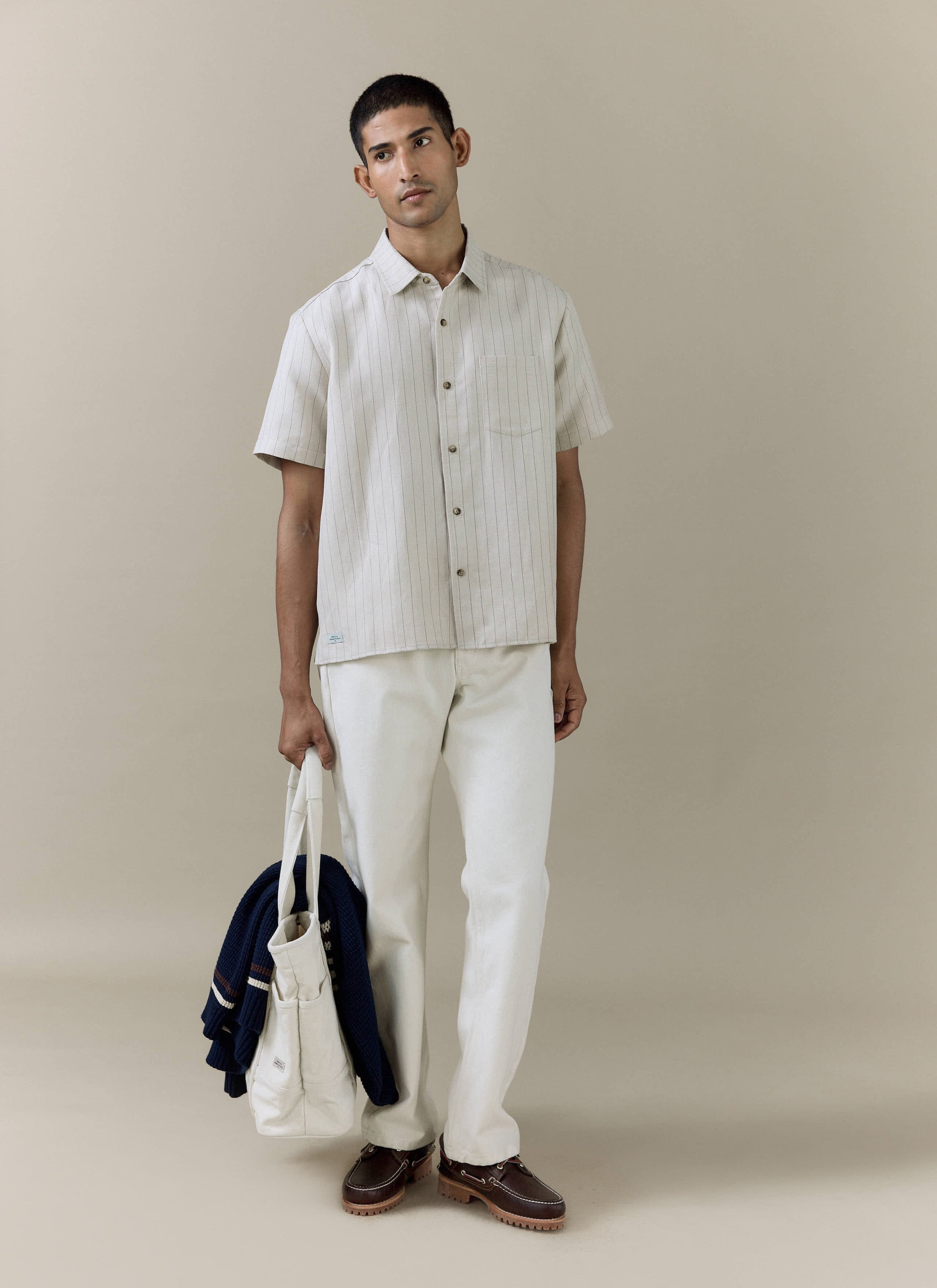 Model wearing the Percival Striped Boxy Shirt in cream pinstripe linen blend, styled with white trousers.