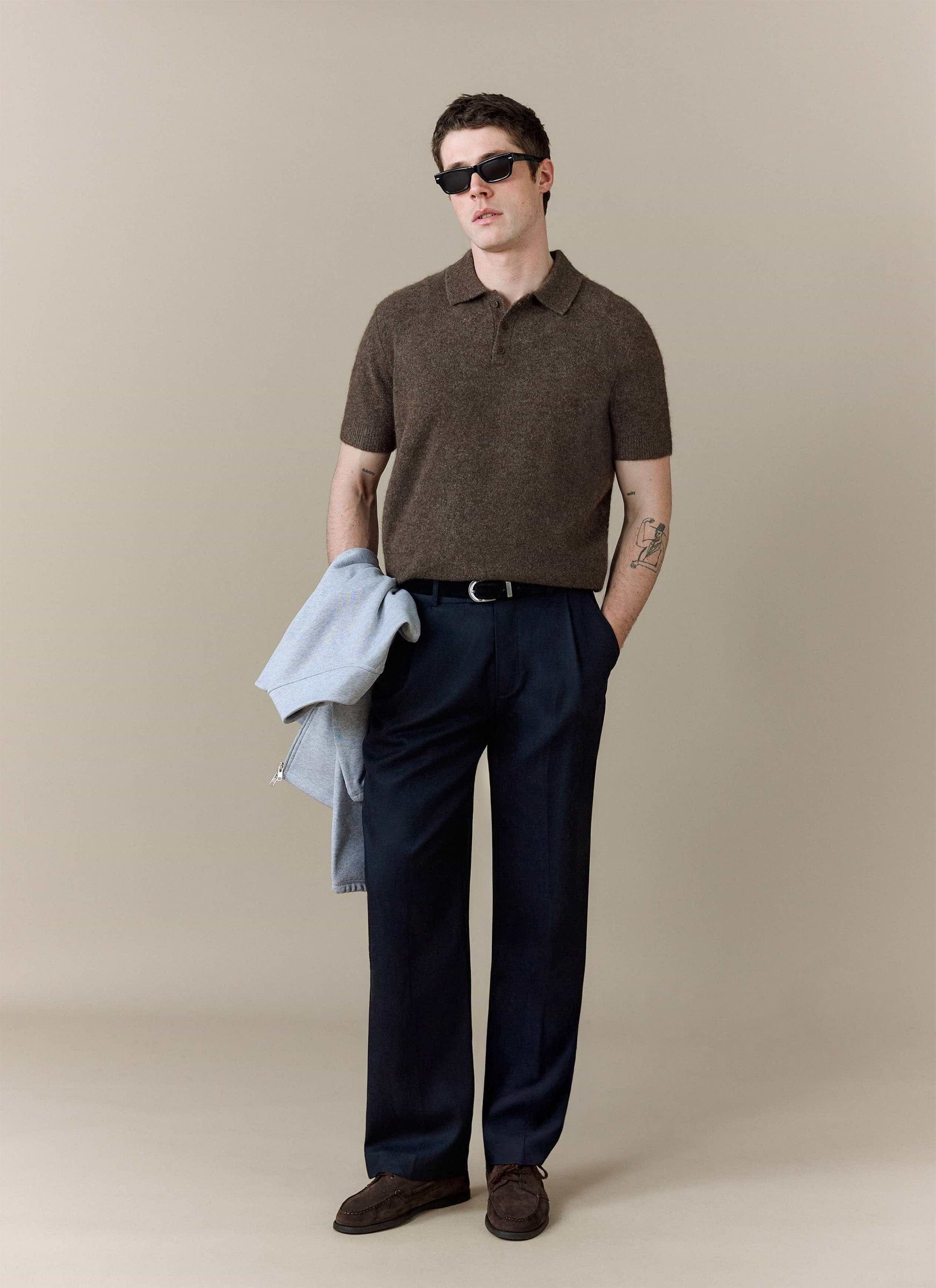 A model wears the Collins Boxy Knitted Polo in Espresso from Percival, styled with dark tailored trousers and sunglasses.