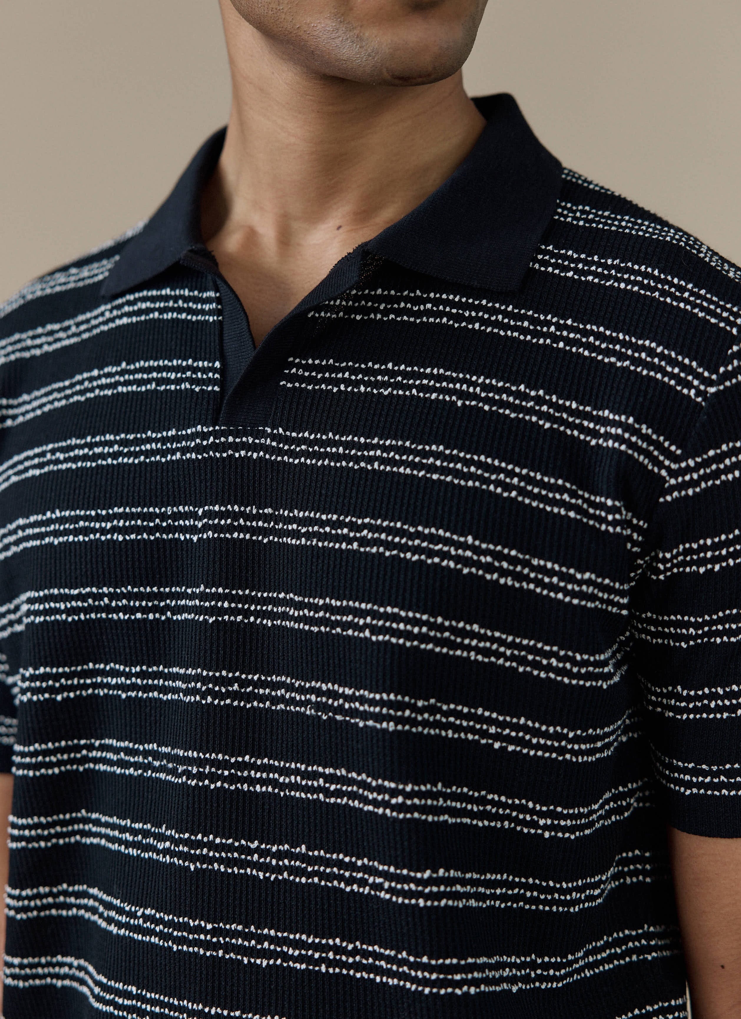 Close-up of the Percival Laurent Polo in black, showing the textured stripe stitch pattern and open collar design.