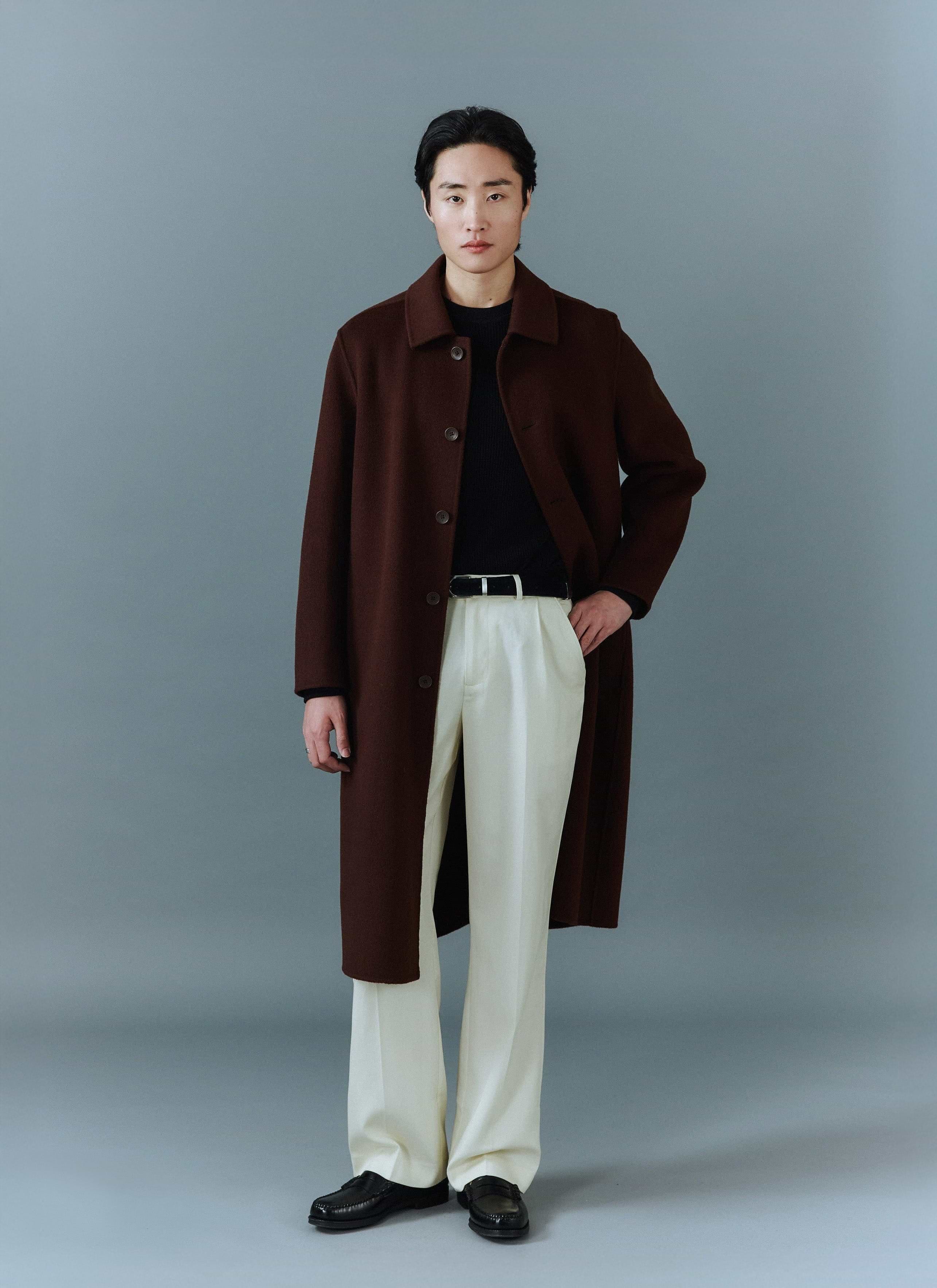 A man models the Percival Minnesota Overcoat in espresso wool, styled with cream trousers and a black knit jumper.
