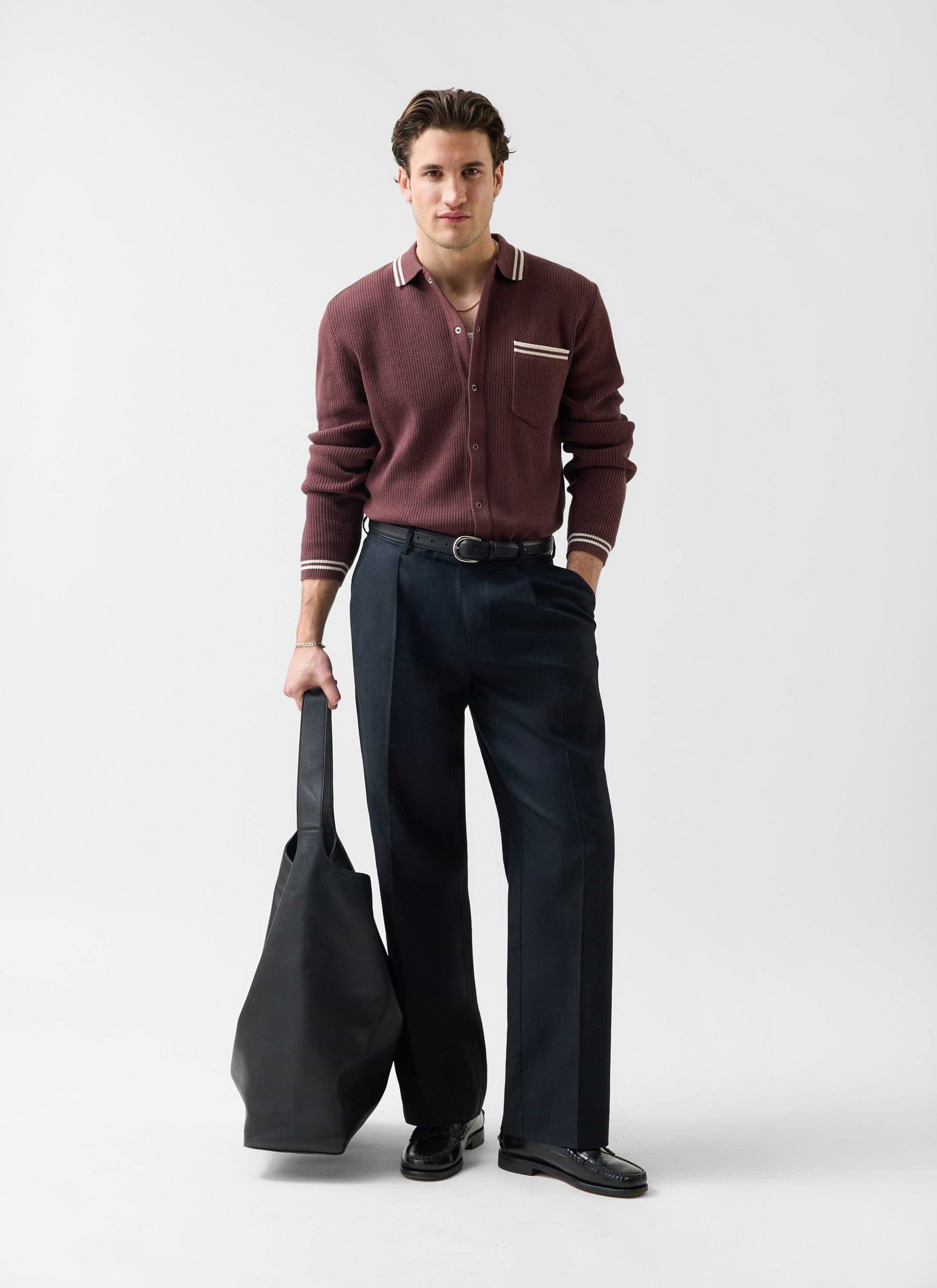 A model wears the Percival Pablo long sleeve knitted cotton shirt in espresso with black trousers and a black bag.