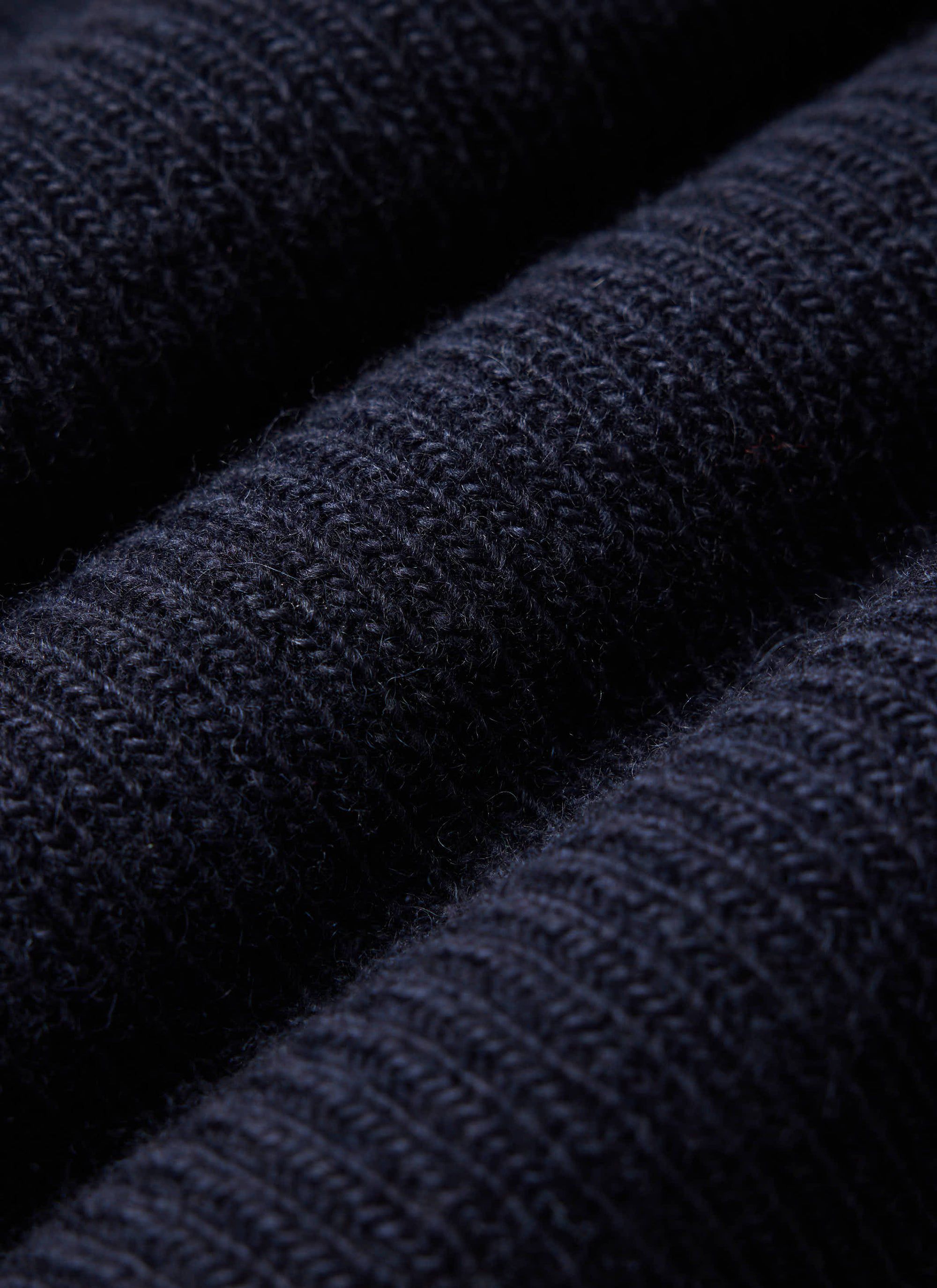 A close-up of the Percival Fisherman Raglan Jumper in navy, highlighting the chunky ribbed texture of the 100% wool knit.