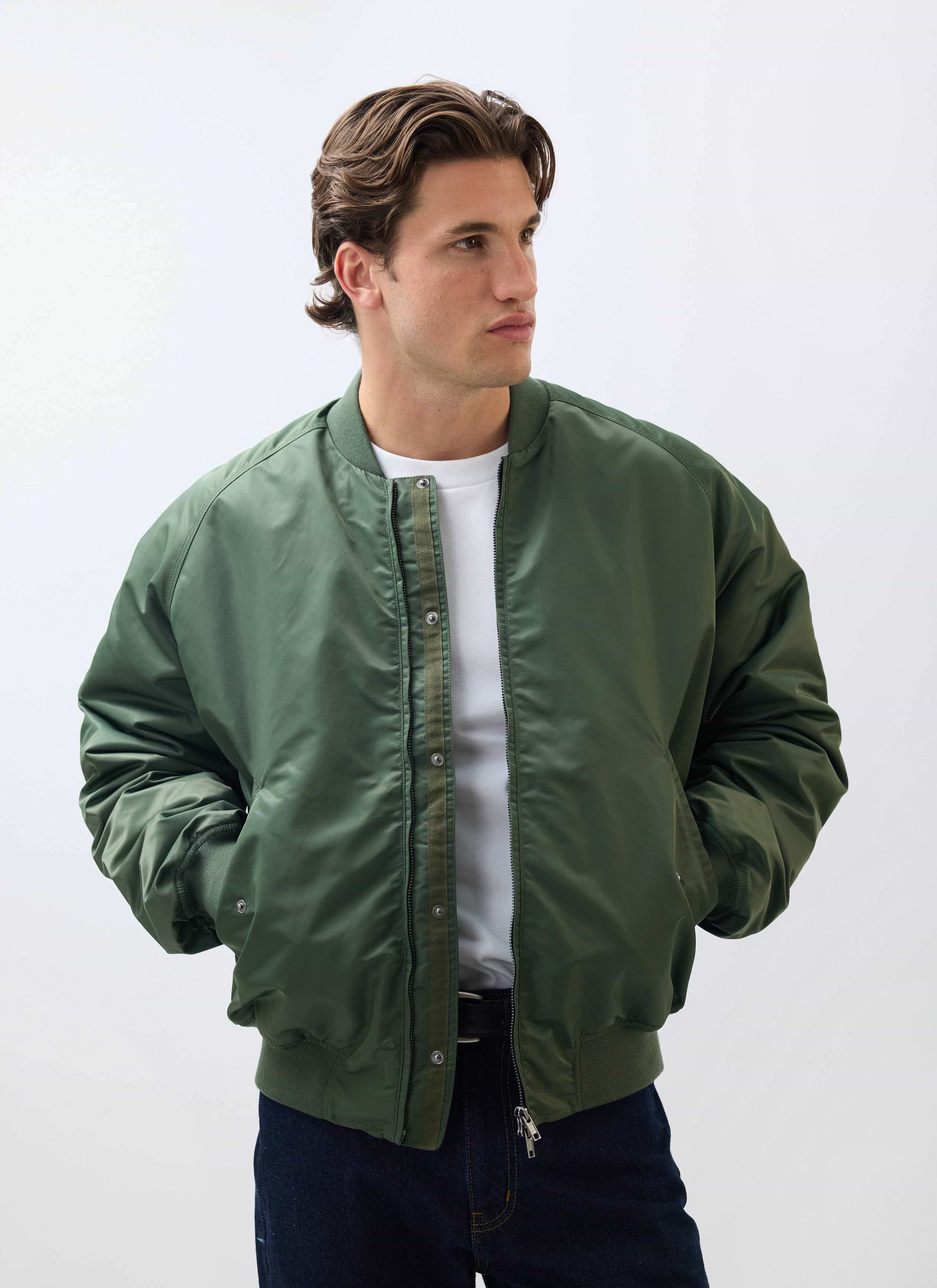 A model wears the Percival Nylon Bomber Jacket in forest green over a white t-shirt against a white studio background.