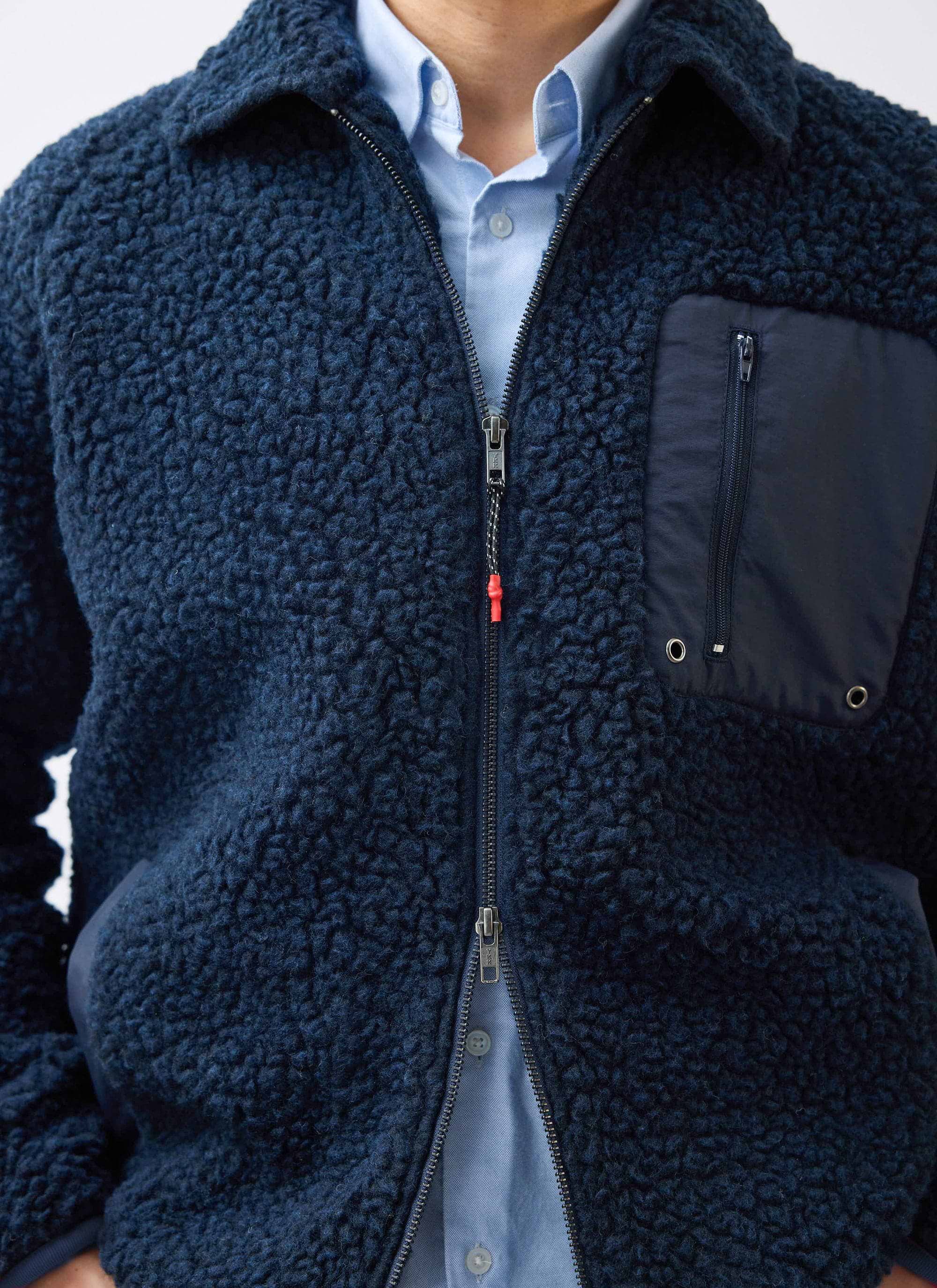 Close up of the navy wool fleece jacket by Percival with zip and pocket detail, worn over a blue shirt.