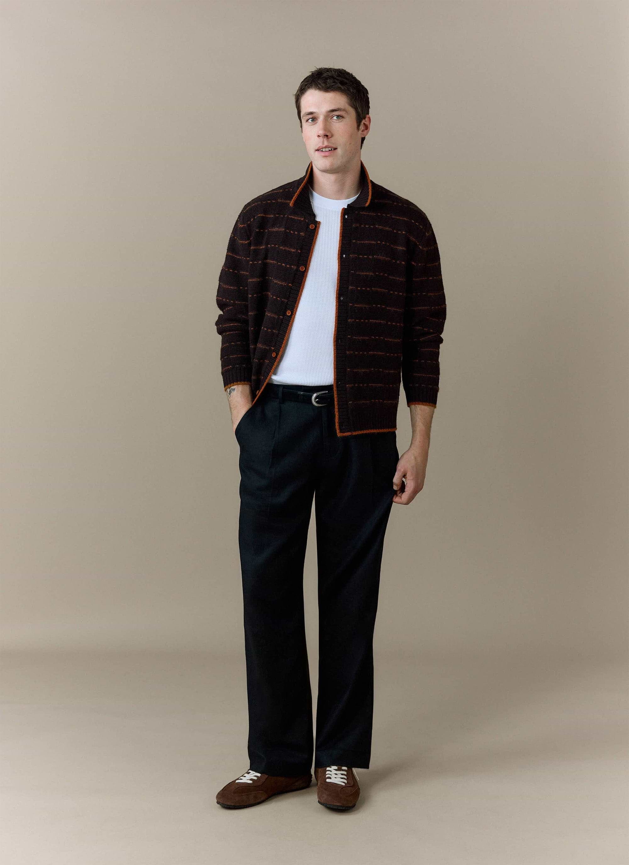A model wears the Percival Addison Long Sleeve Knitted Shirt in brown, styled open over a white t-shirt and black trousers.
