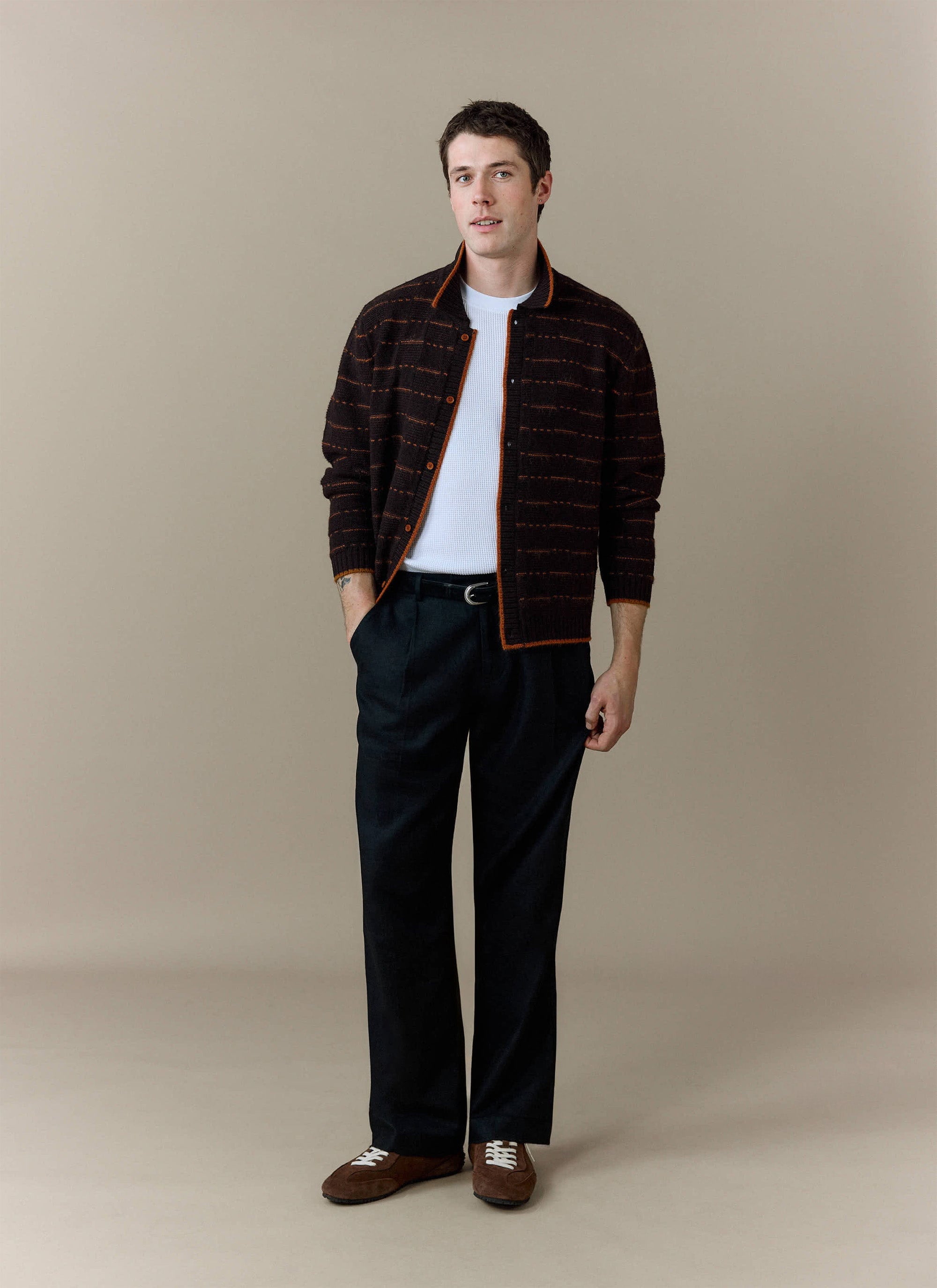 A model wears the Percival Addison Long Sleeve Knitted Shirt in brown, styled open over a white t-shirt and black trousers.