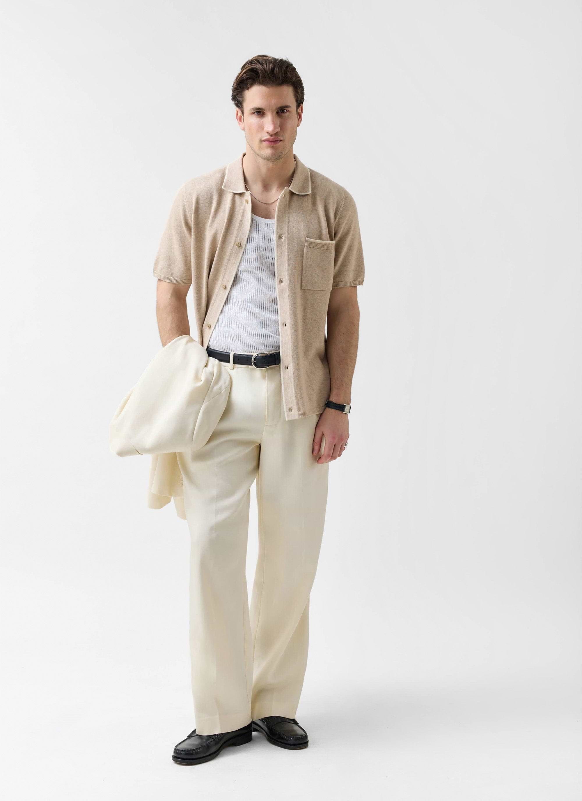 A man models the Percival beige wool-blend knitted shirt, styled open over a vest with cream trousers.