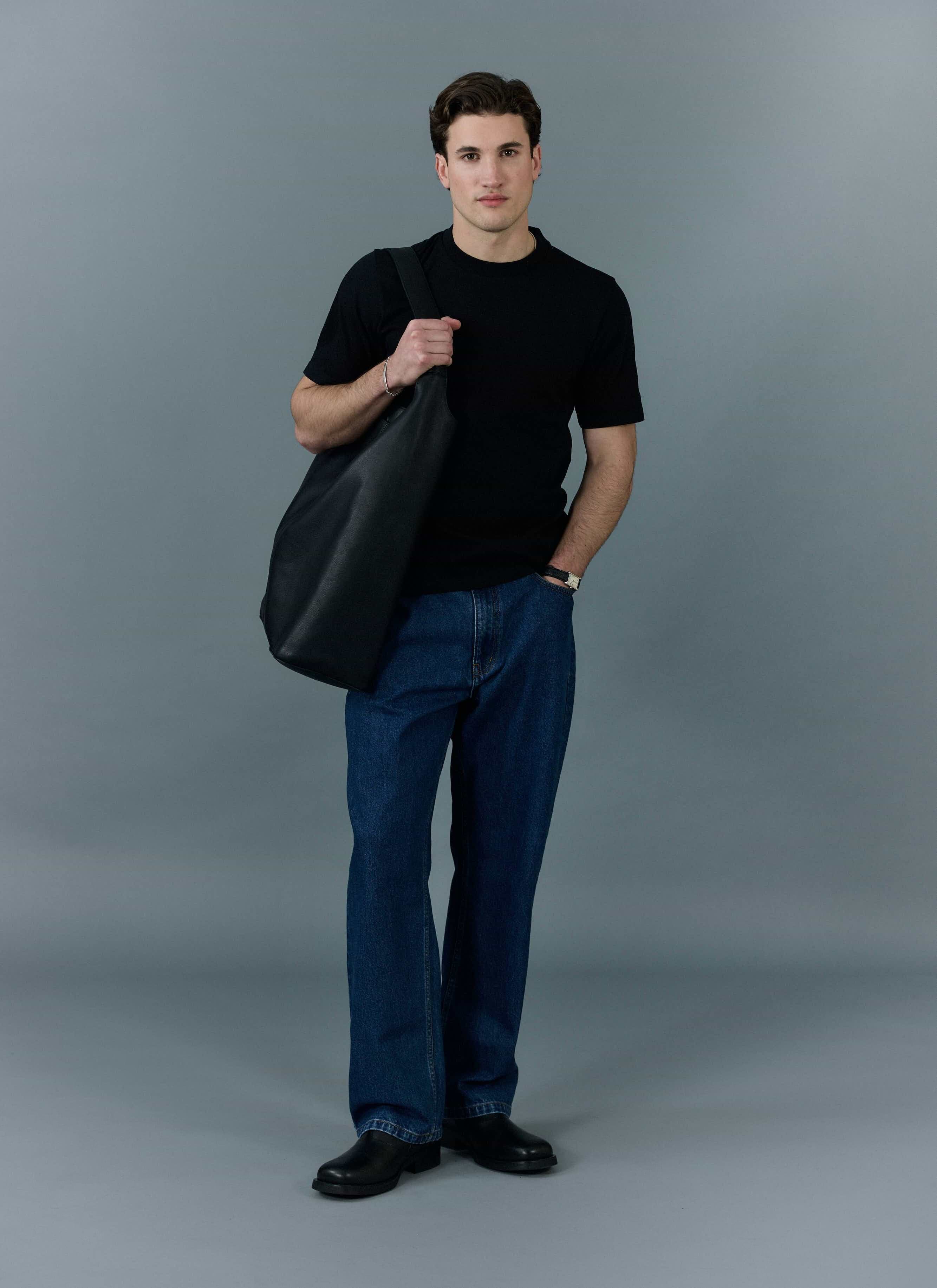 A model wears the Percival Cropped Regular Fit T Shirt in black with dark blue jeans and a large black tote bag.