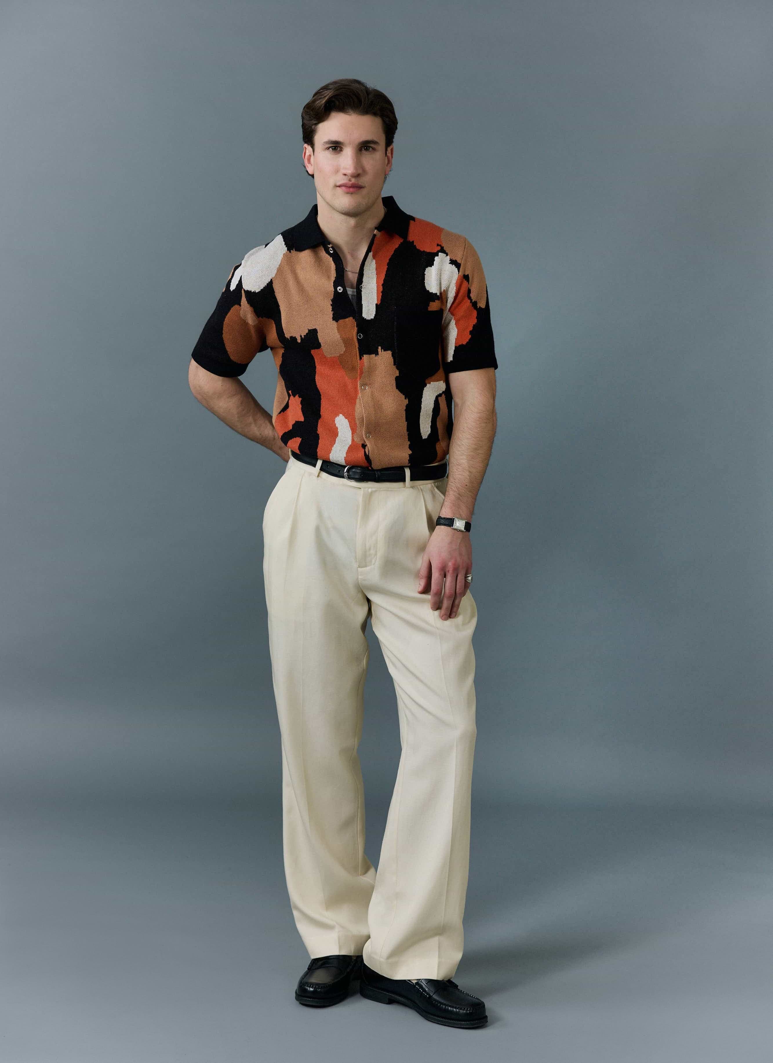 A model wears the Percival Impressionist Jacquard Shirt in a black multi-colour pattern with cream trousers and black shoes.