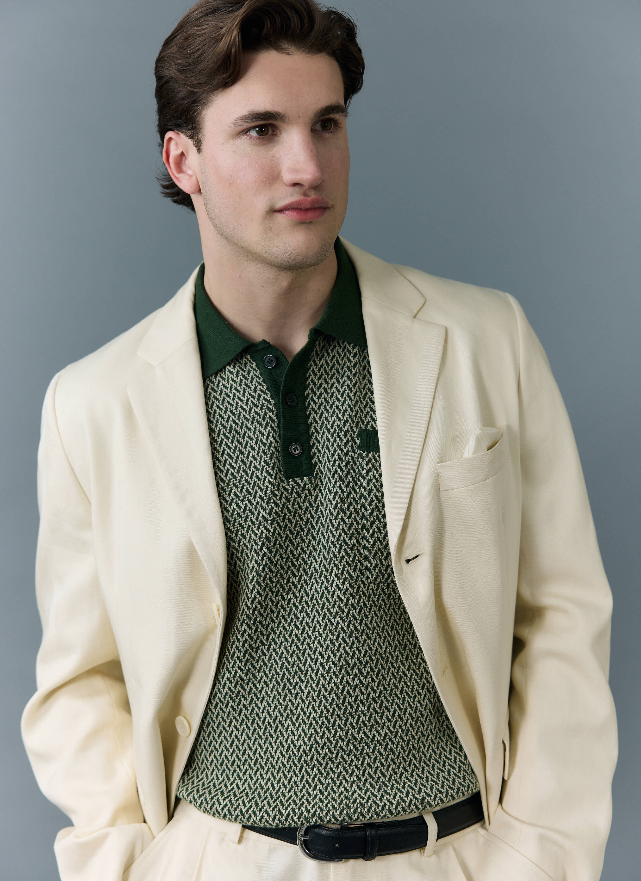 A man wears the green patterned Casa Martini Knitted Polo by Percival, layered underneath a smart cream suit jacket.