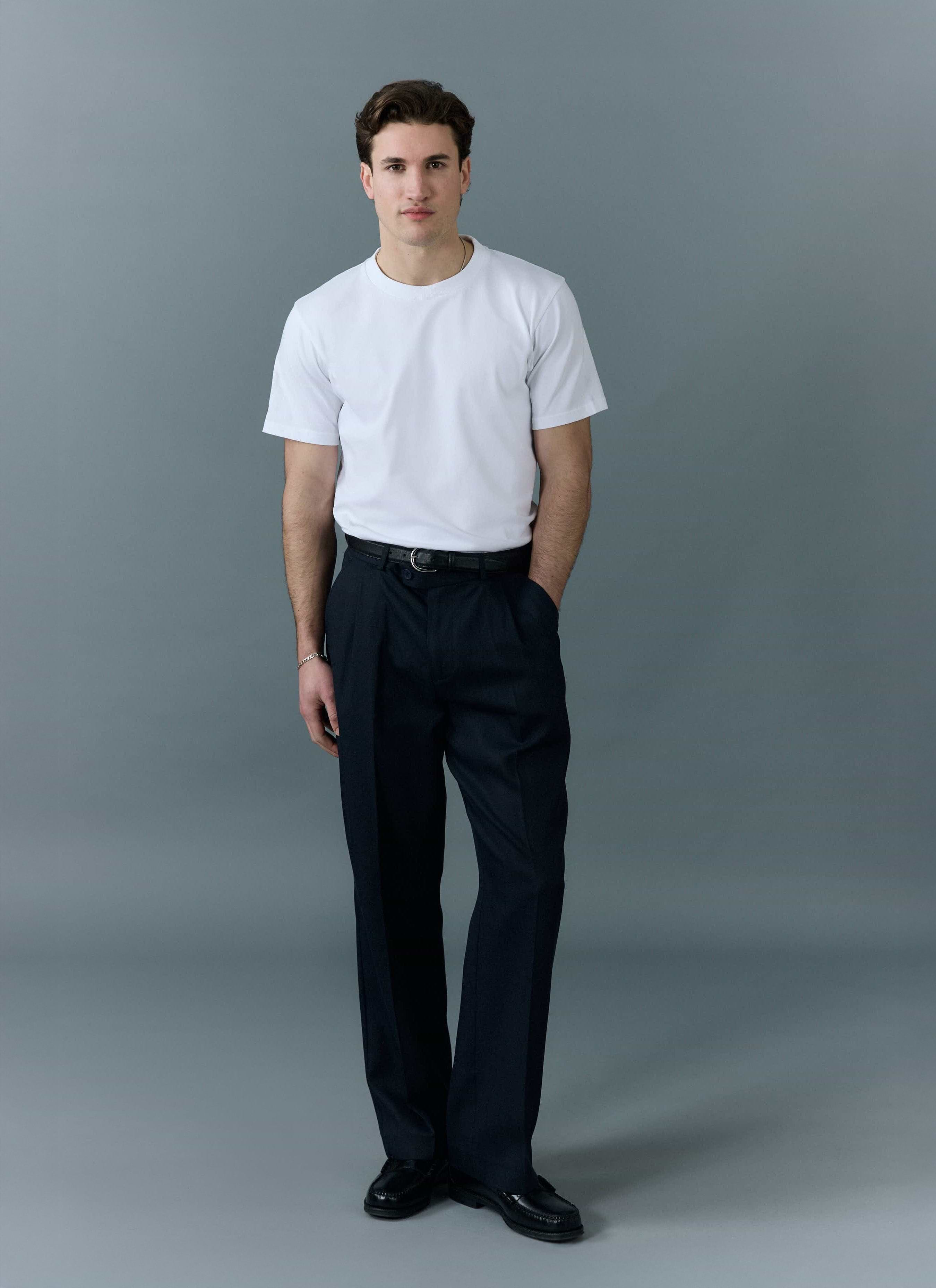 a model wears a percival plain white t shirt with dark trousers and loafers