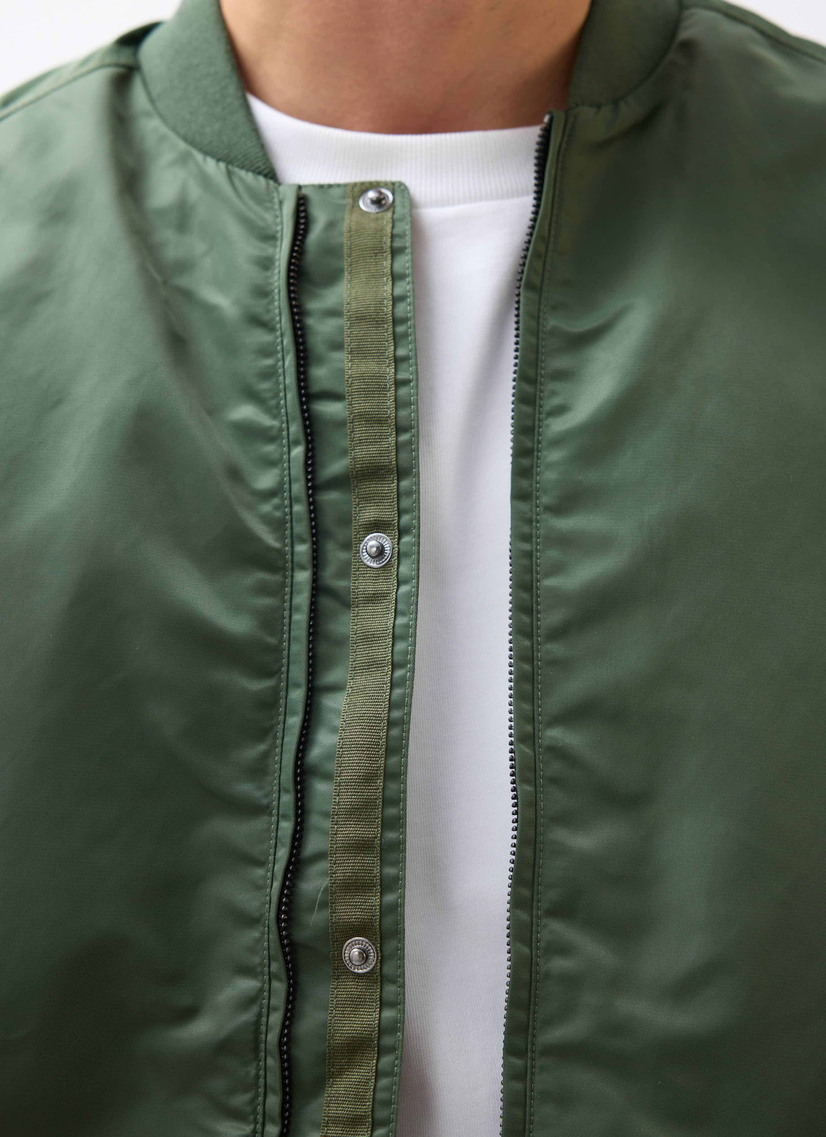 A close-up of the Percival Nylon Bomber Jacket in forest green, showing the zip and button placket detail.