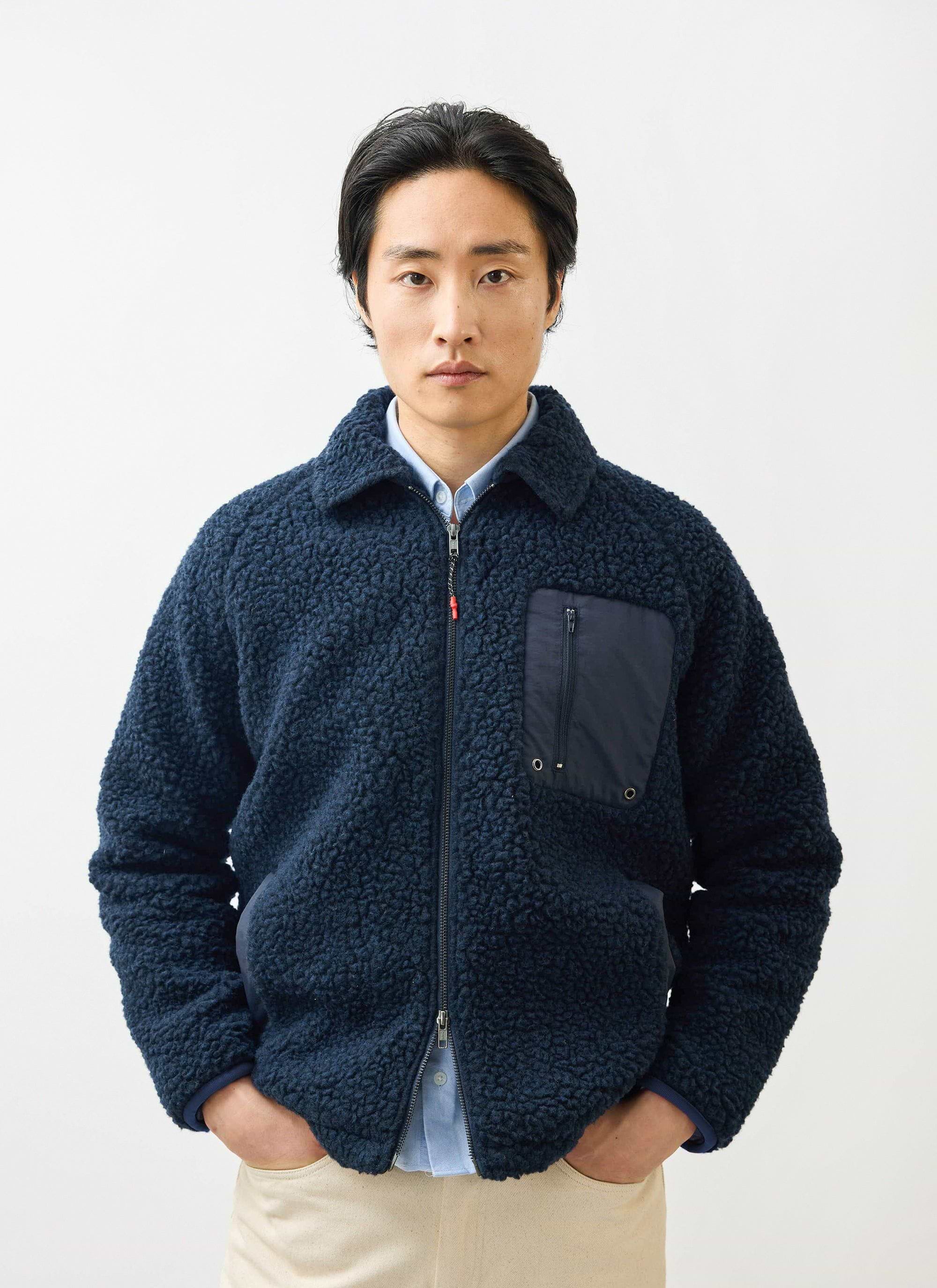 A model wears the Percival navy wool fleece jacket. The zip-up jacket features a chest pocket and is worn over a blue shirt.