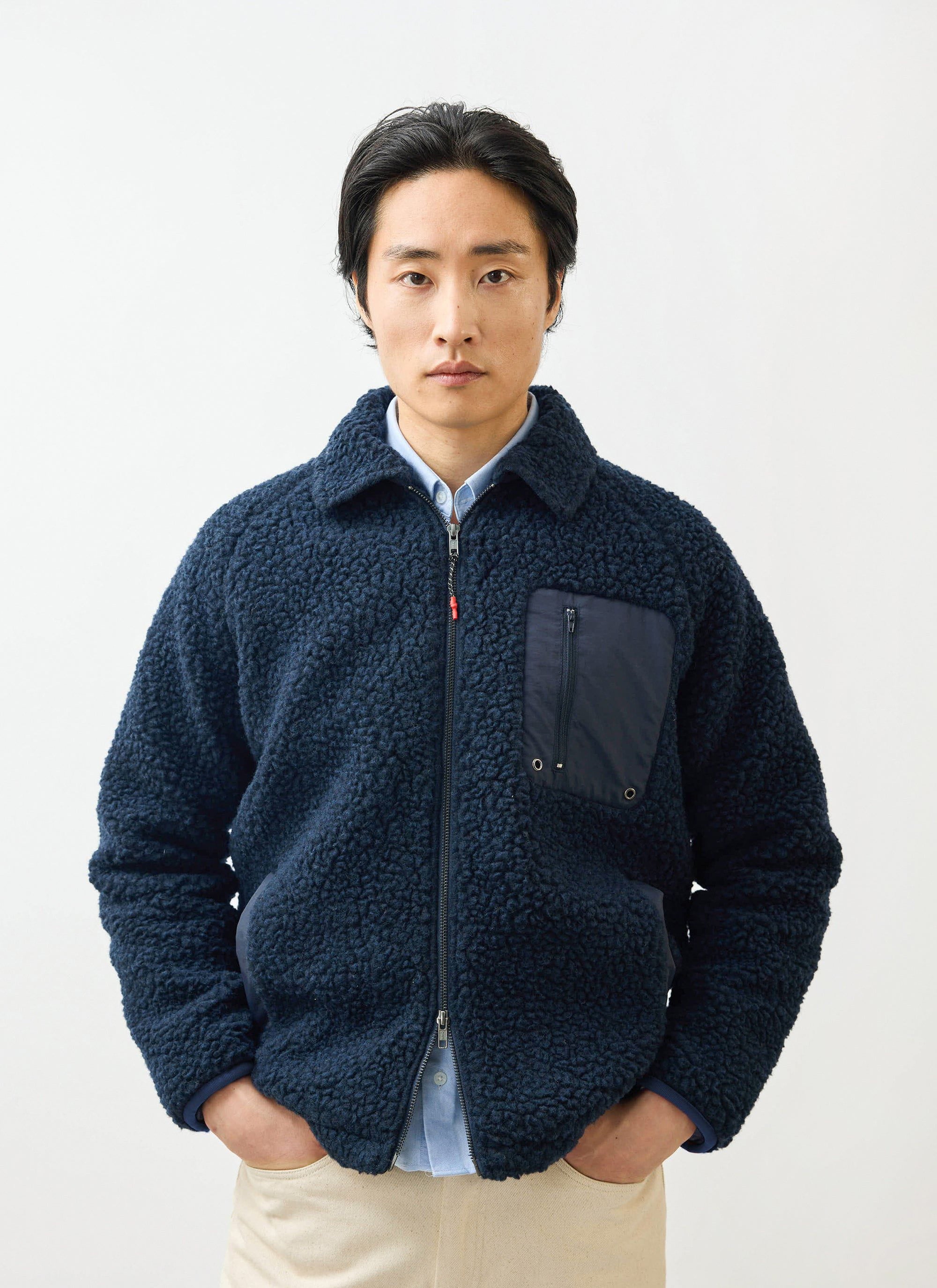 A model wears the Percival navy wool fleece jacket. The zip-up jacket features a chest pocket and is worn over a blue shirt.
