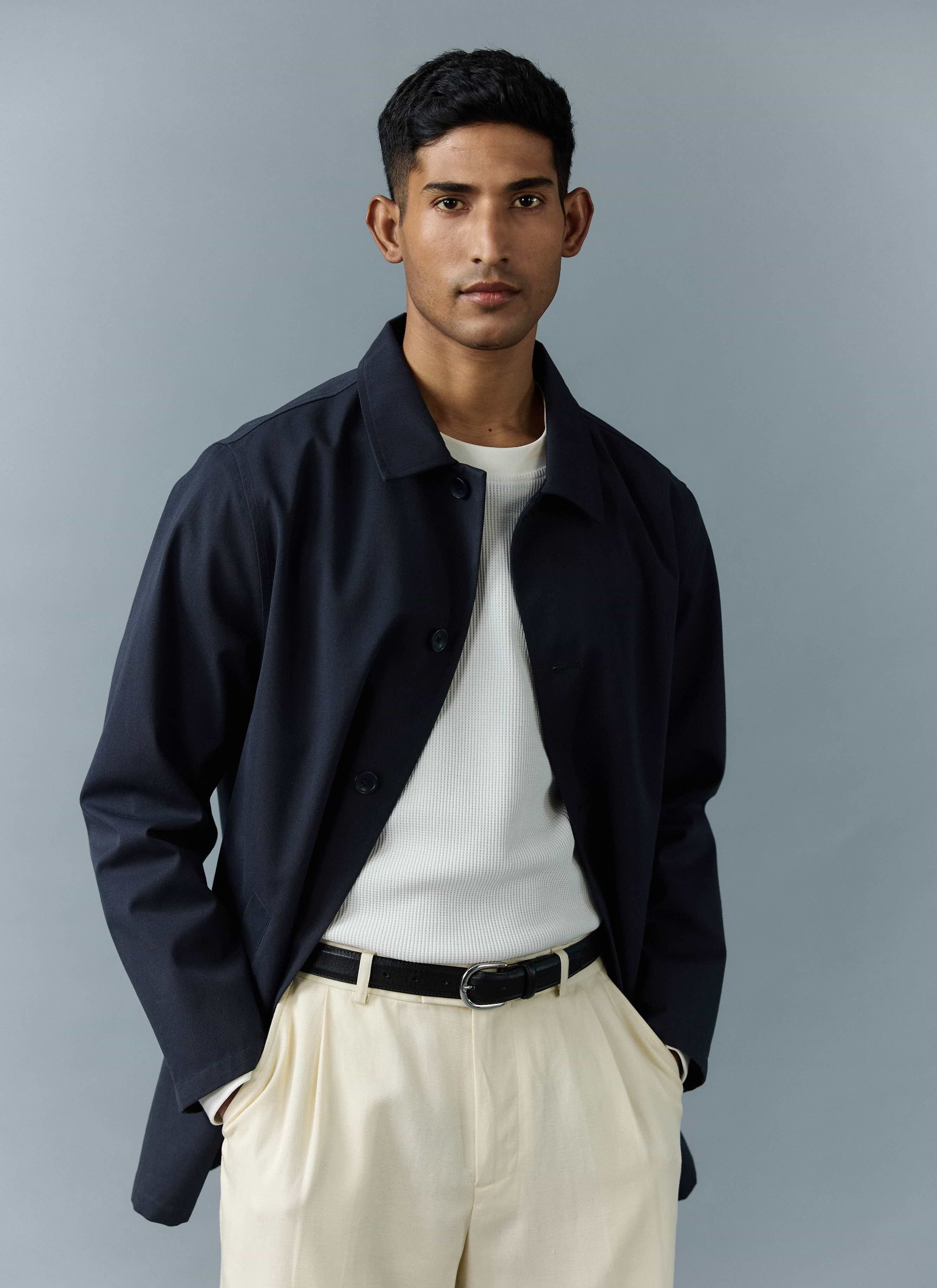 A model wears the Percival Men's Navy Sherlock Short Trench Coat, styled open over a white top and cream trousers.