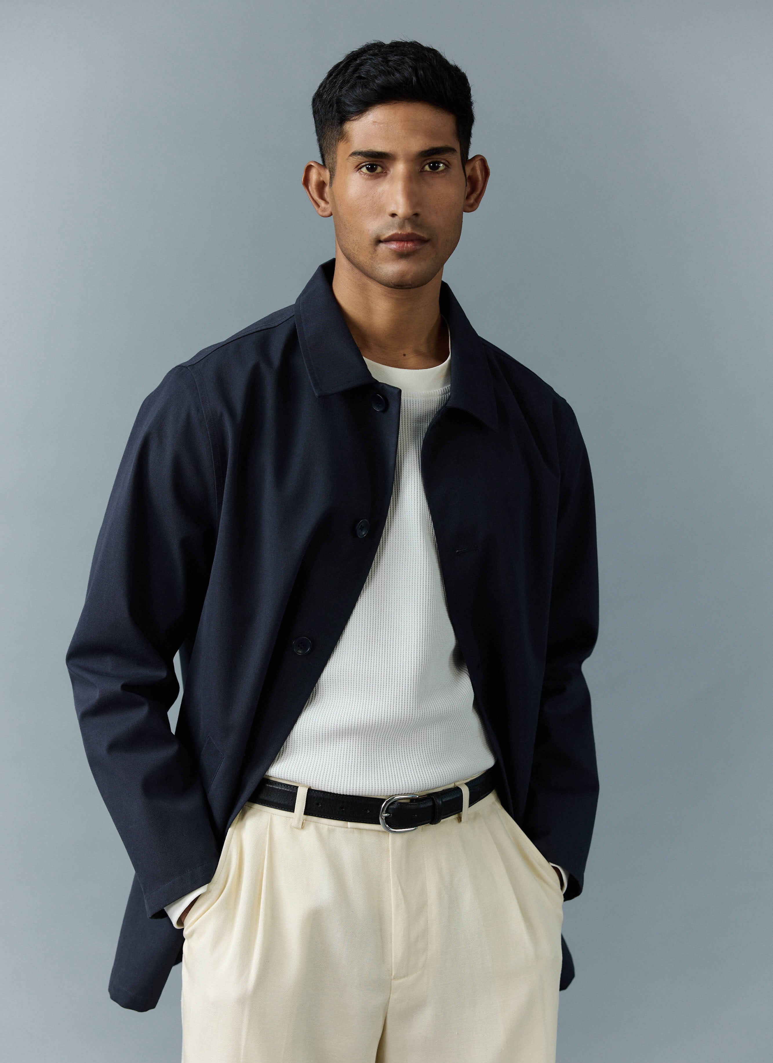 A model wears the Percival Men's Navy Sherlock Short Trench Coat, styled open over a white top and cream trousers.