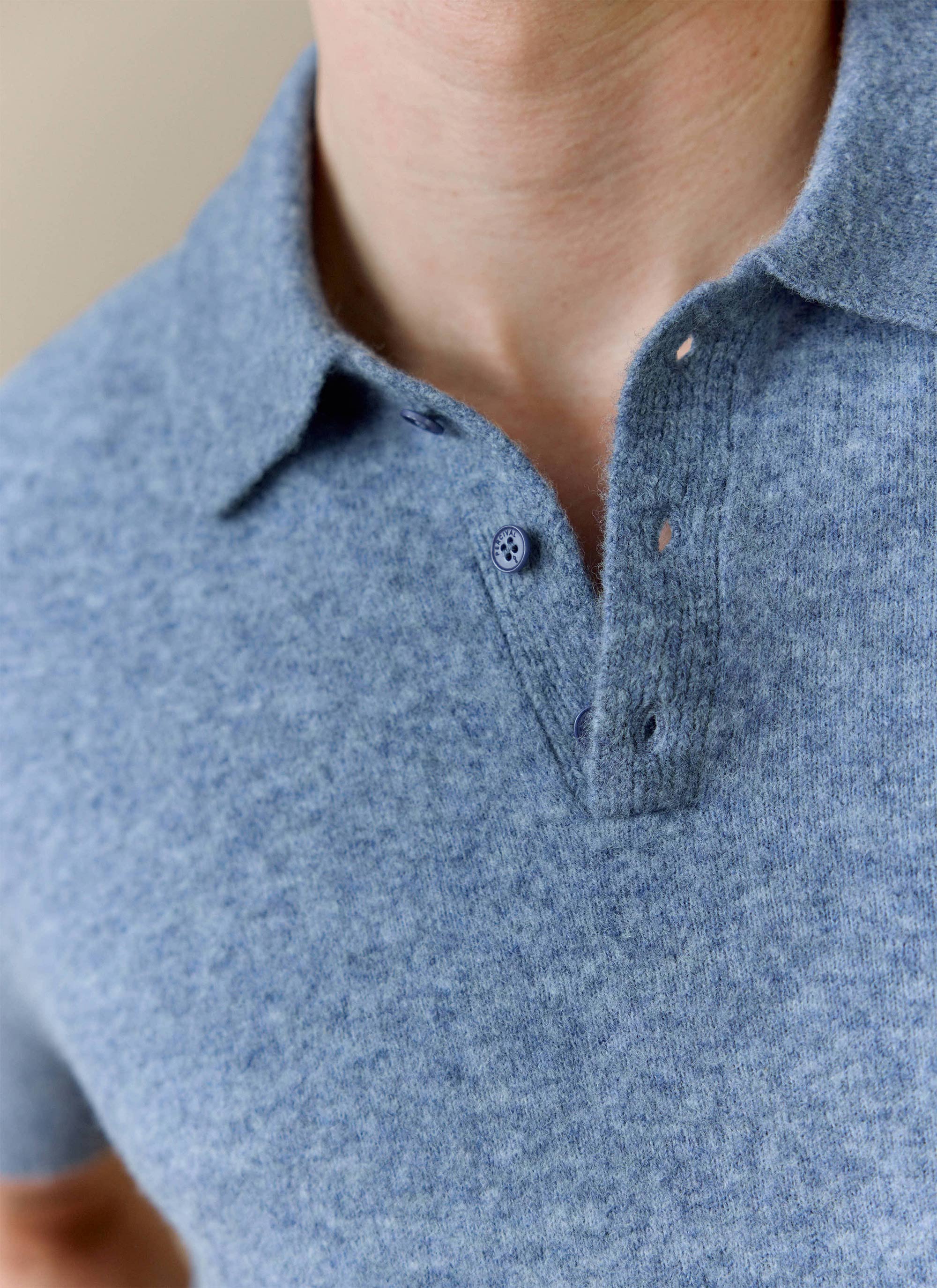 Close up of the Percival Collins Boxy Knitted Polo in blue, showing the soft yak blend fabric and branded button detail.