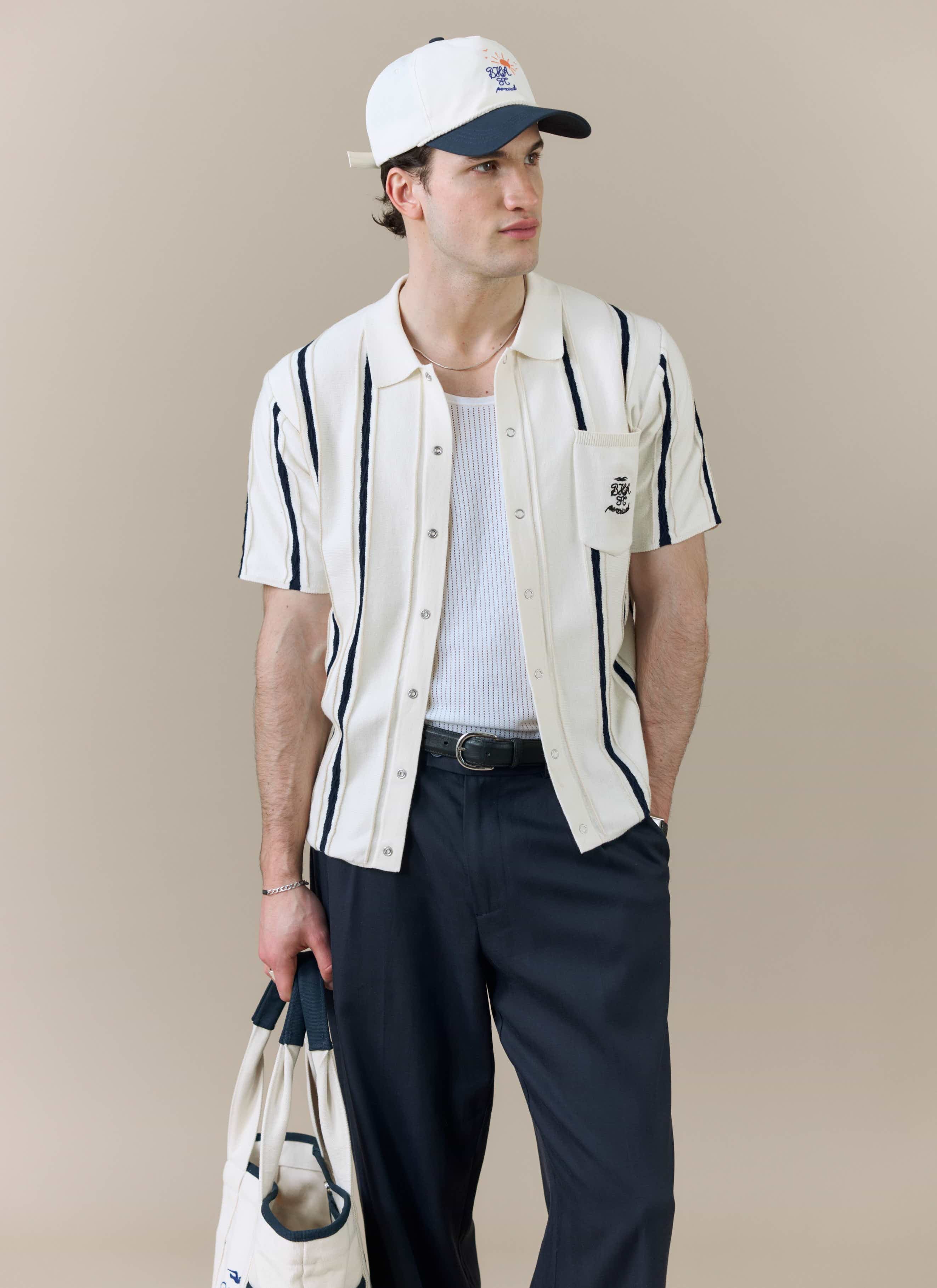 A model wears the Percival x Brighton & Hove Albion F.C. Cable Stripe Knitted Shirt in white, styled with a cap and tote bag.
