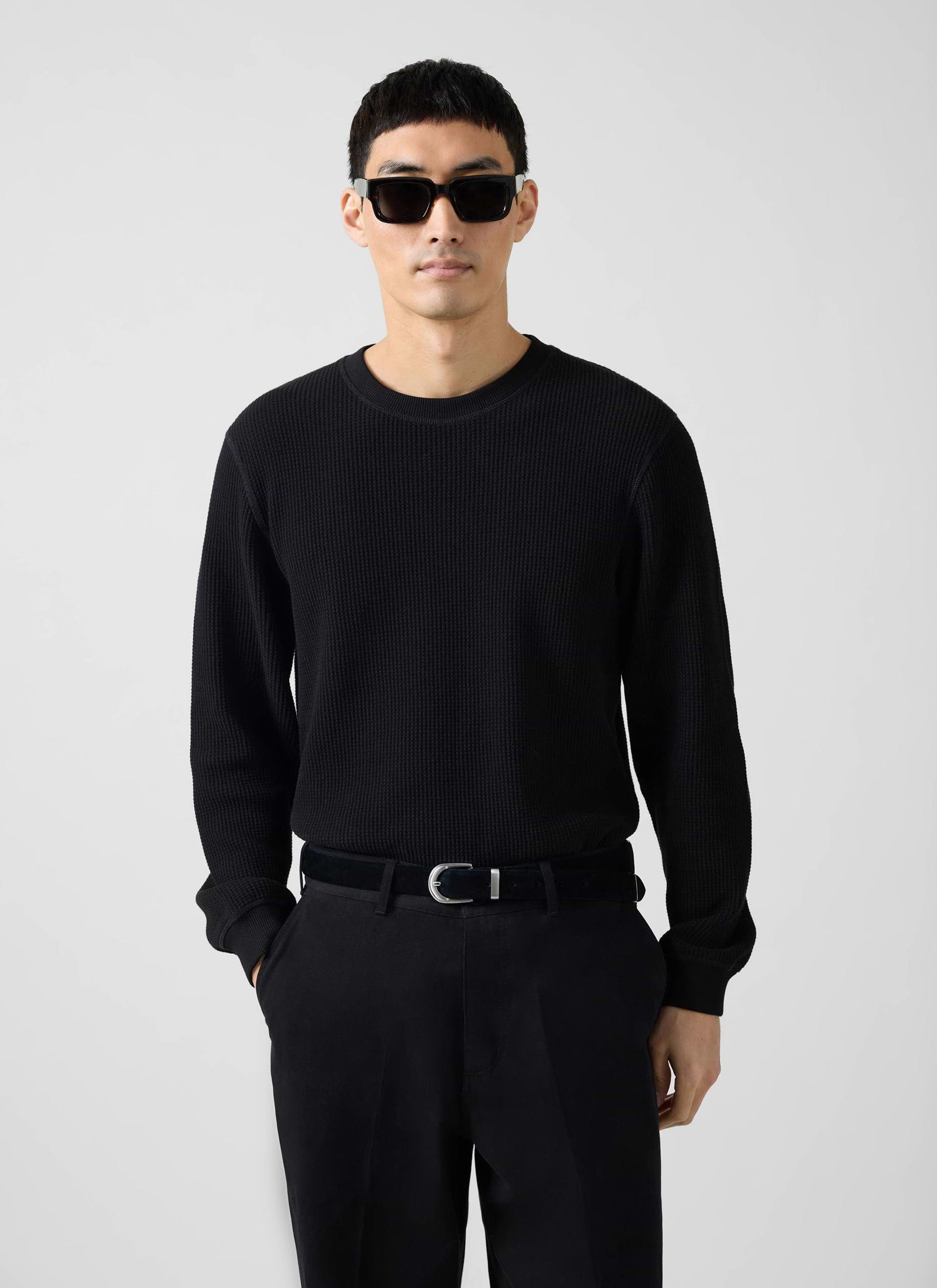 A man models the Percival black Waffle Long Sleeve T Shirt, styled with black trousers and sunglasses.