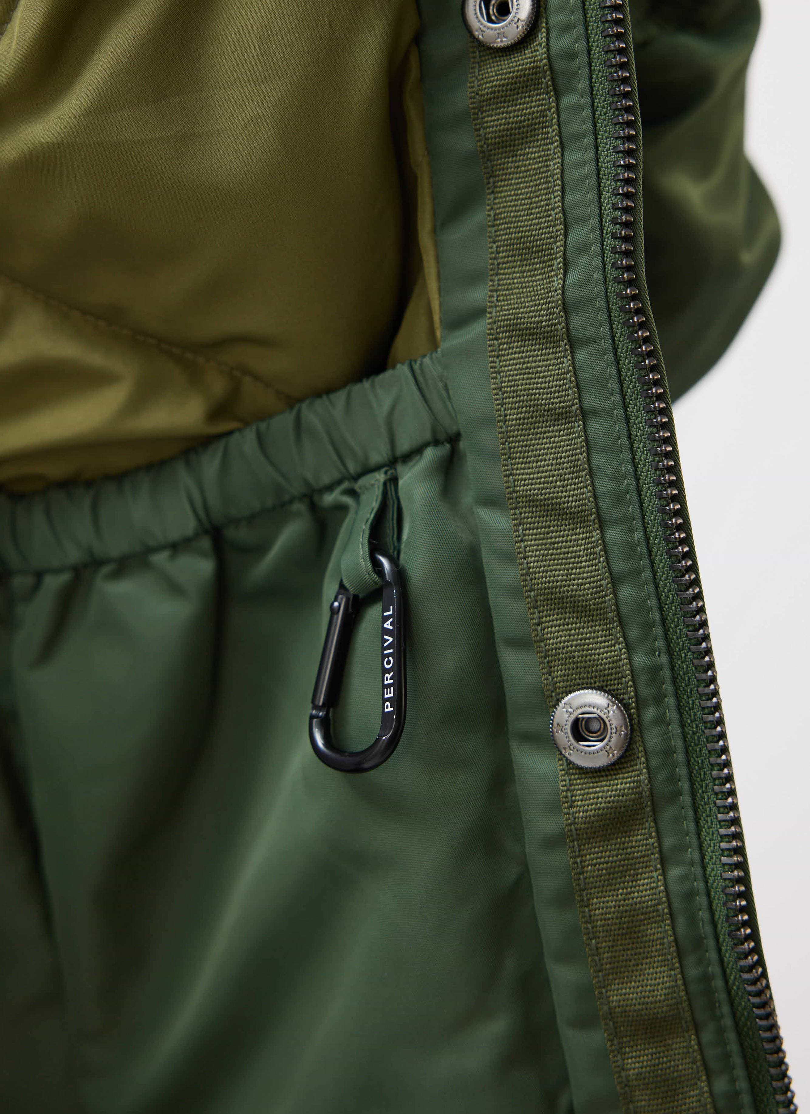 A close-up of the Percival branded carabiner clip inside the pocket of the forest green nylon bomber jacket.