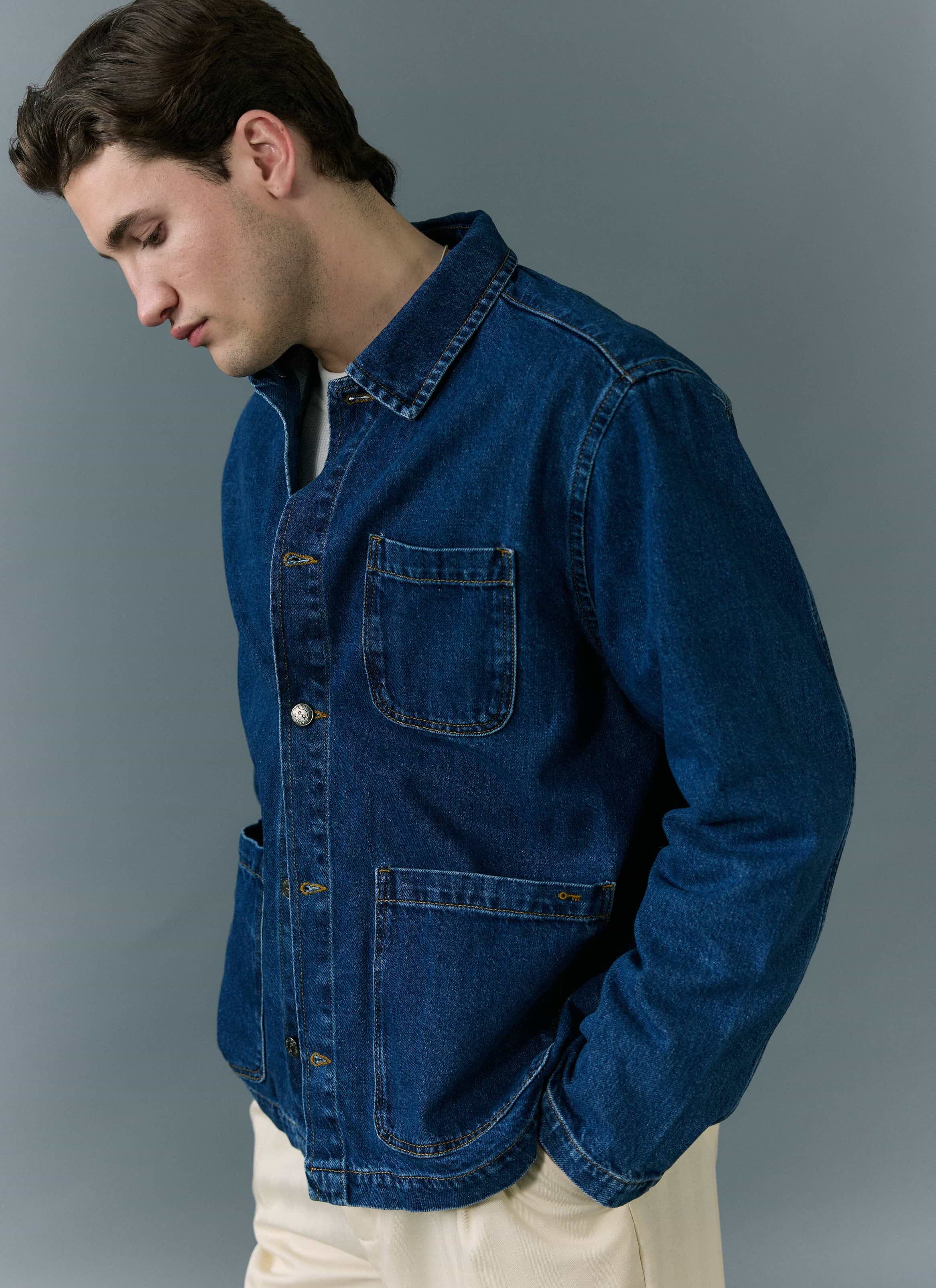 A model wears the Percival Gove Chore Jacket in mid wash blue denim, standing against a grey background.