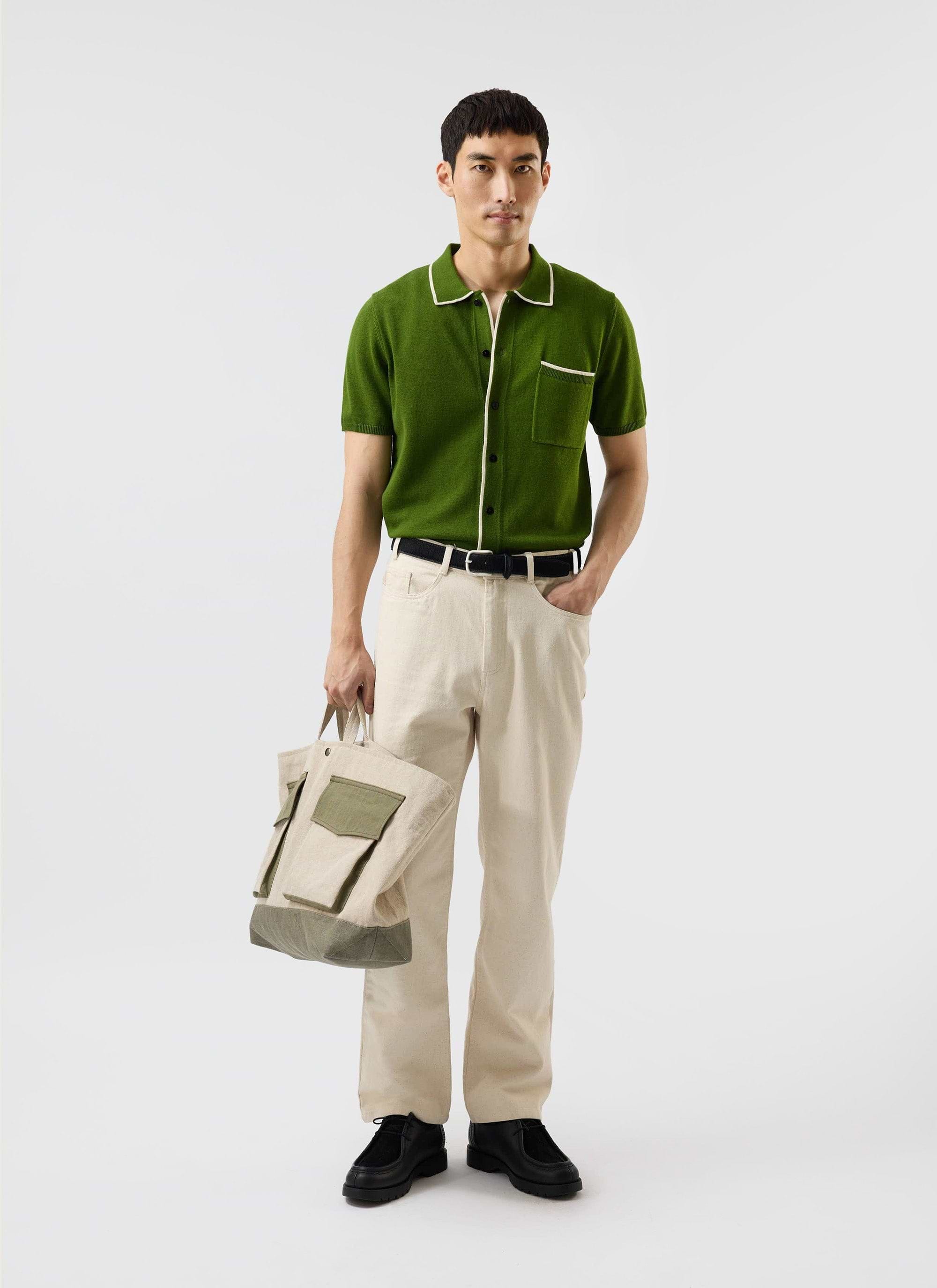 A man models the Percival Contrast Trim Shirt in forest green, styled with cream trousers and holding a tote bag.