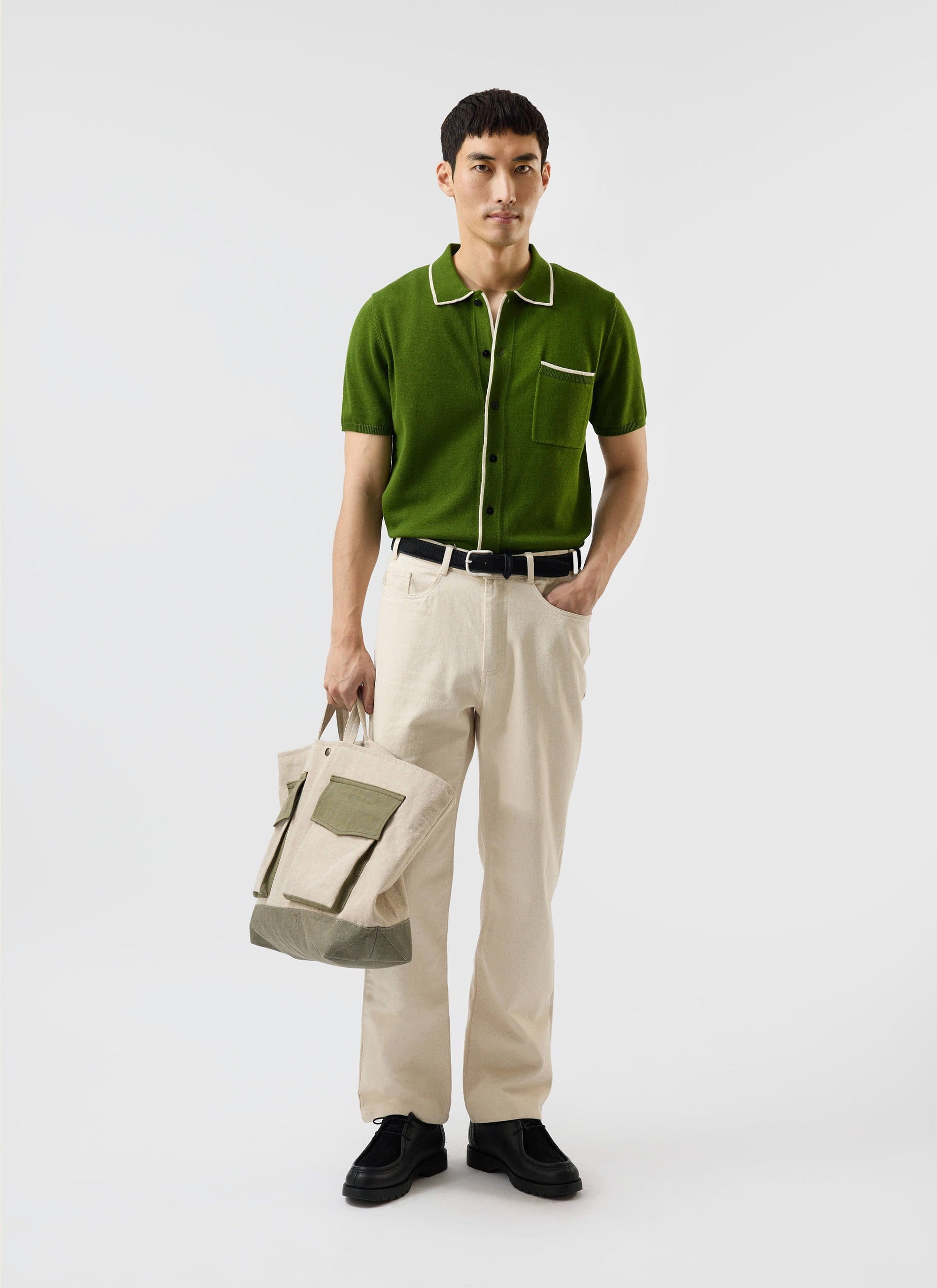 A man models the Percival Contrast Trim Shirt in forest green, styled with cream trousers and holding a tote bag.