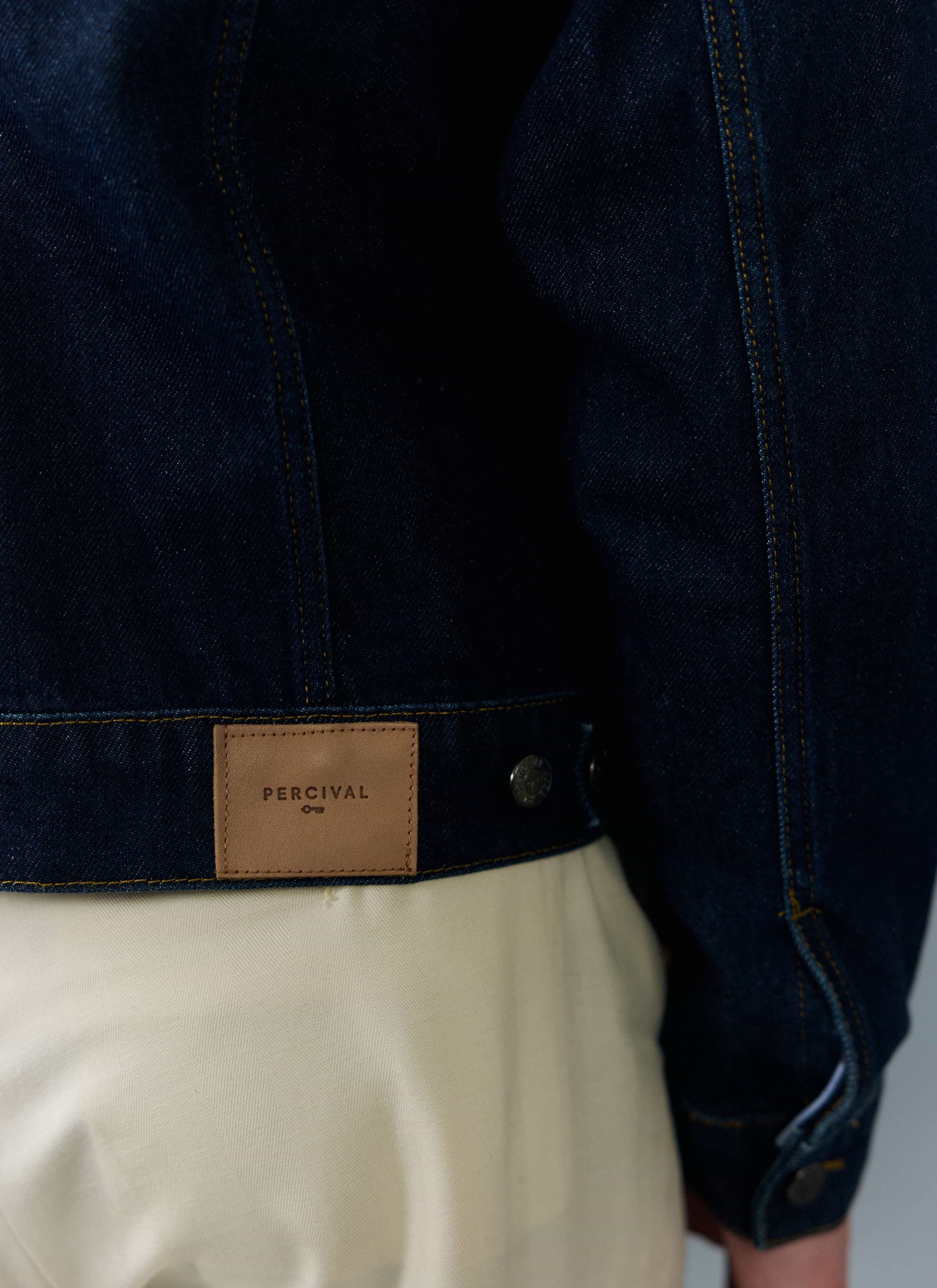 Close-up of a model wearing the Percival Western Trucker Jacket, showing the branded leather patch on the dark indigo denim.