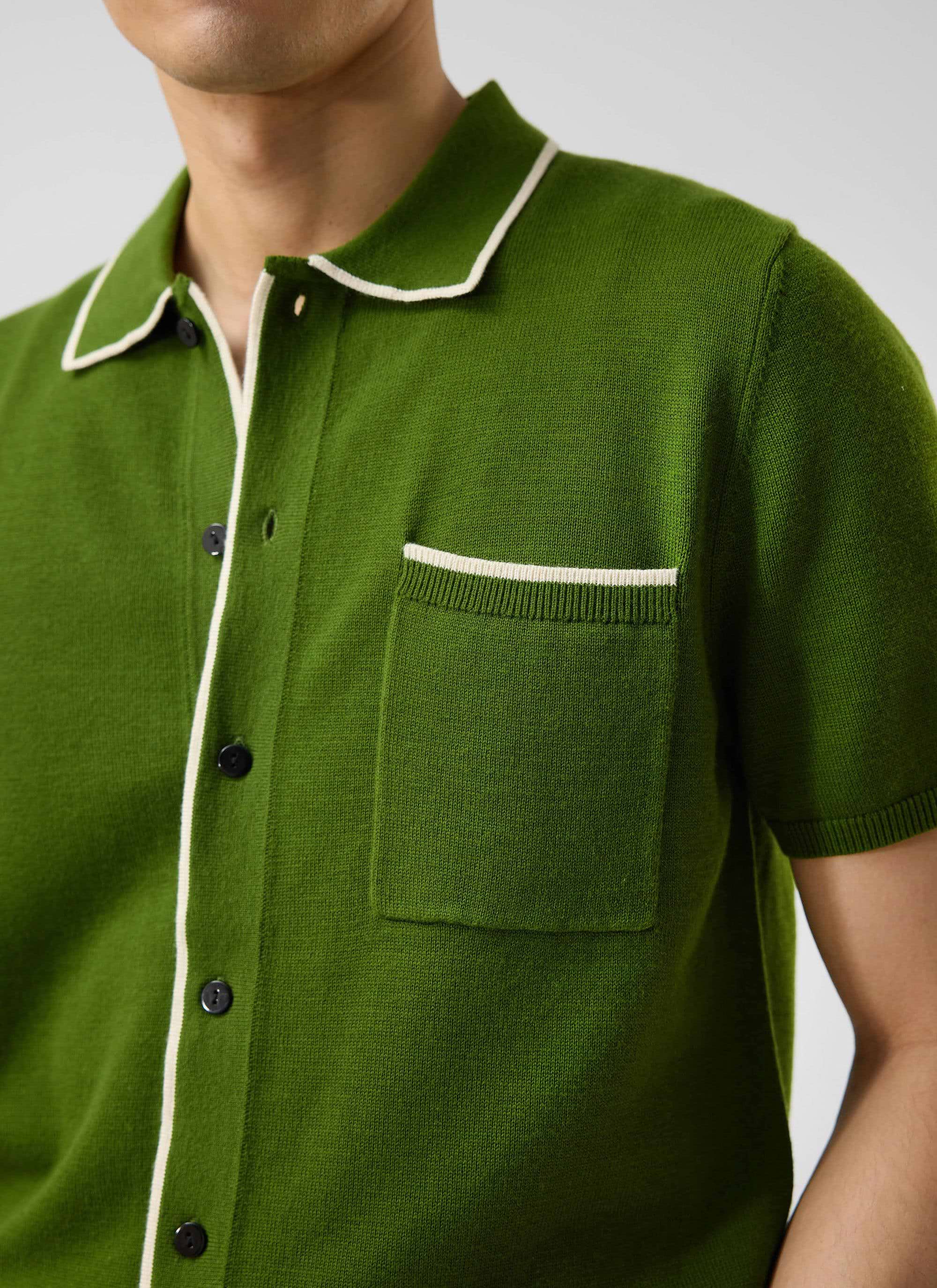 Close-up of a model wearing Percival's Contrast Trim Shirt in forest green, showing the ecru piping on collar and pocket.