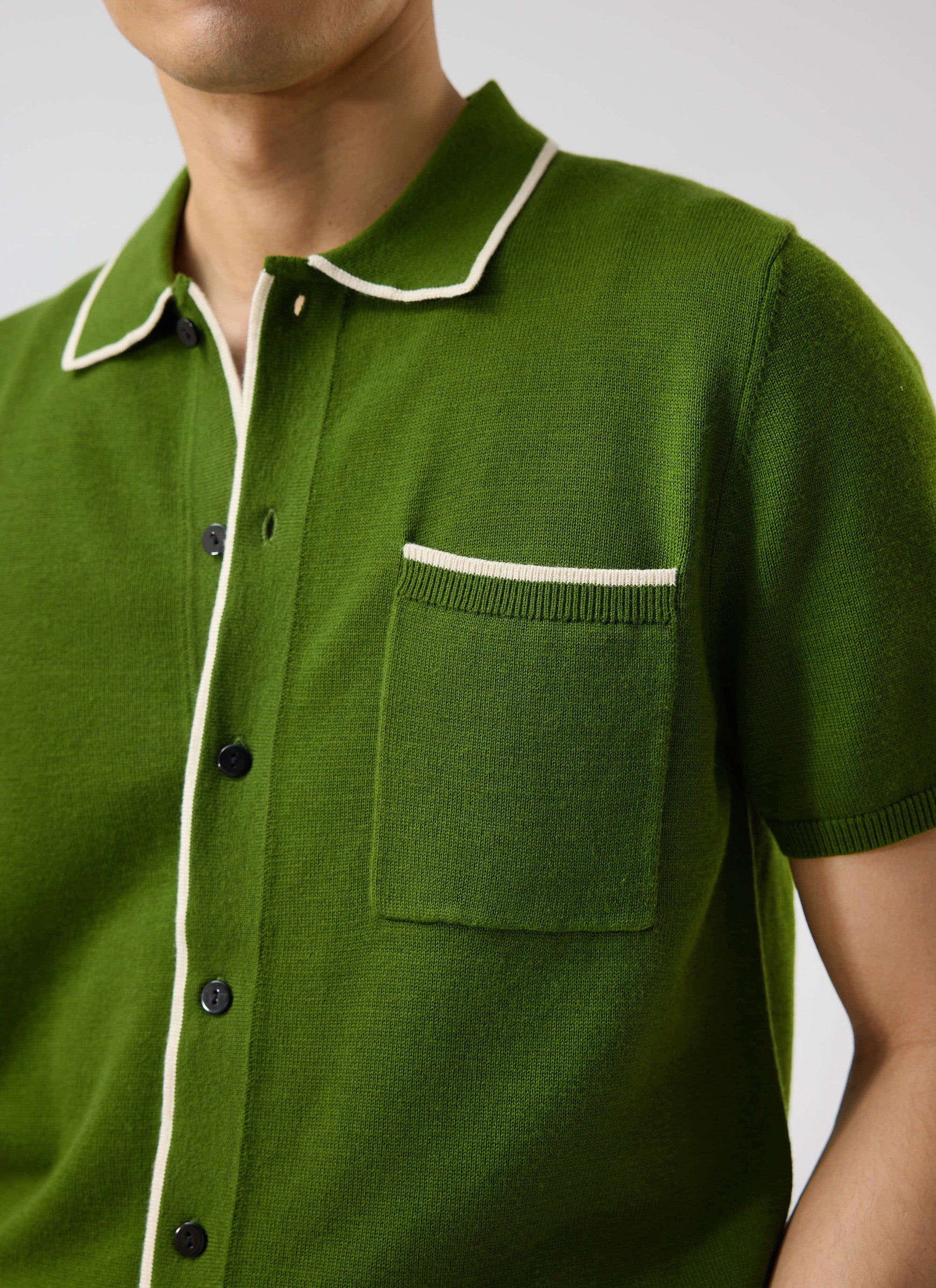 Close-up of a model wearing Percival's Contrast Trim Shirt in forest green, showing the ecru piping on collar and pocket.
