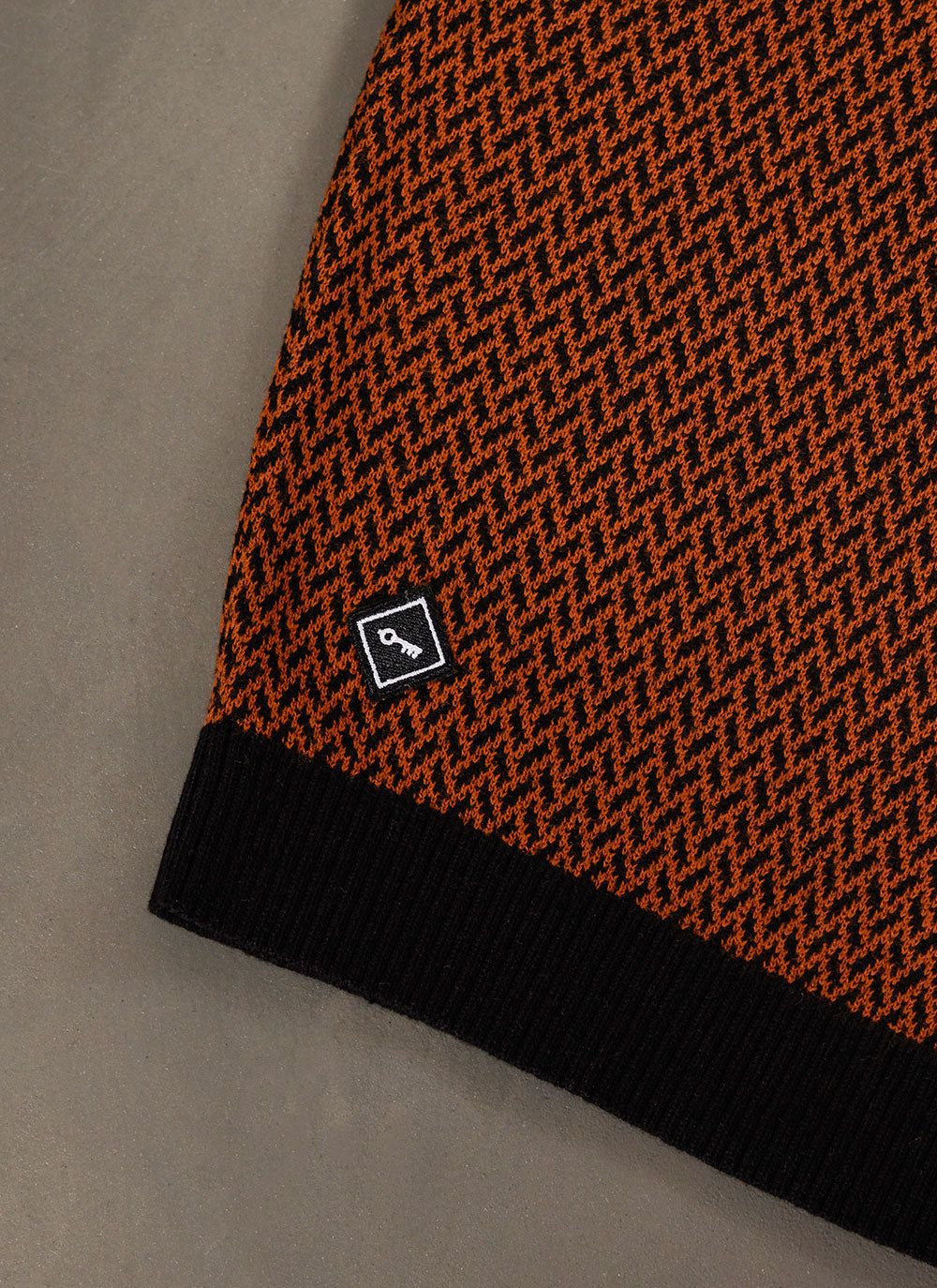 Close up of the Percival Casa Martini Knitted Polo in espresso and black showing the geometric knit pattern and logo tab.