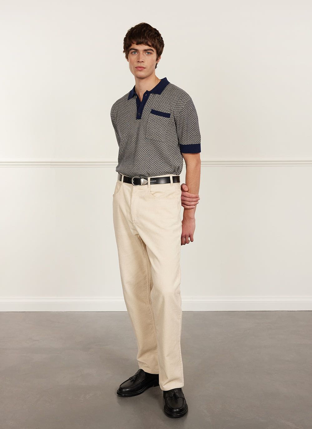 A model wears the Percival Casa Martini Knitted Polo in Navy with cream corduroy trousers and black loafers.