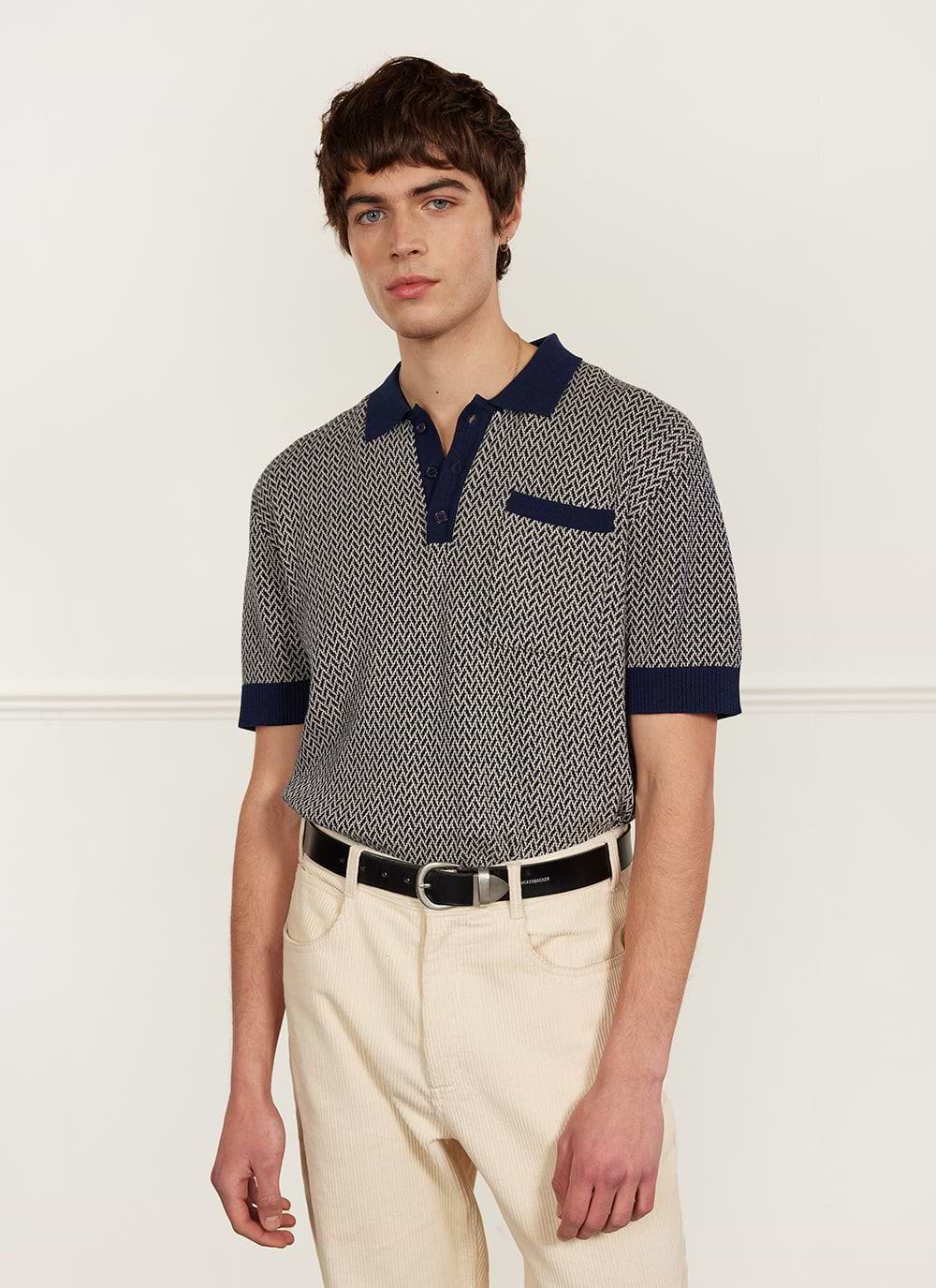 A model wears the Percival Casa Martini Knitted Polo in navy with a chevron pattern, styled with cream trousers.