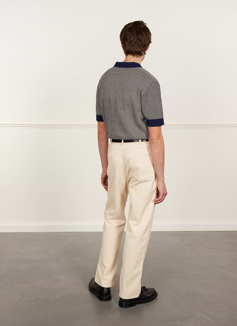 Back view of a model wearing the navy Percival Casa Martini knitted polo shirt with cream trousers and black shoes.