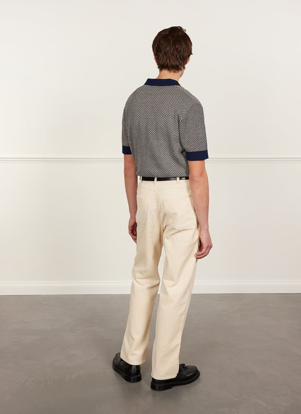 Back view of a model wearing the navy Percival Casa Martini knitted polo shirt with cream trousers and black shoes.