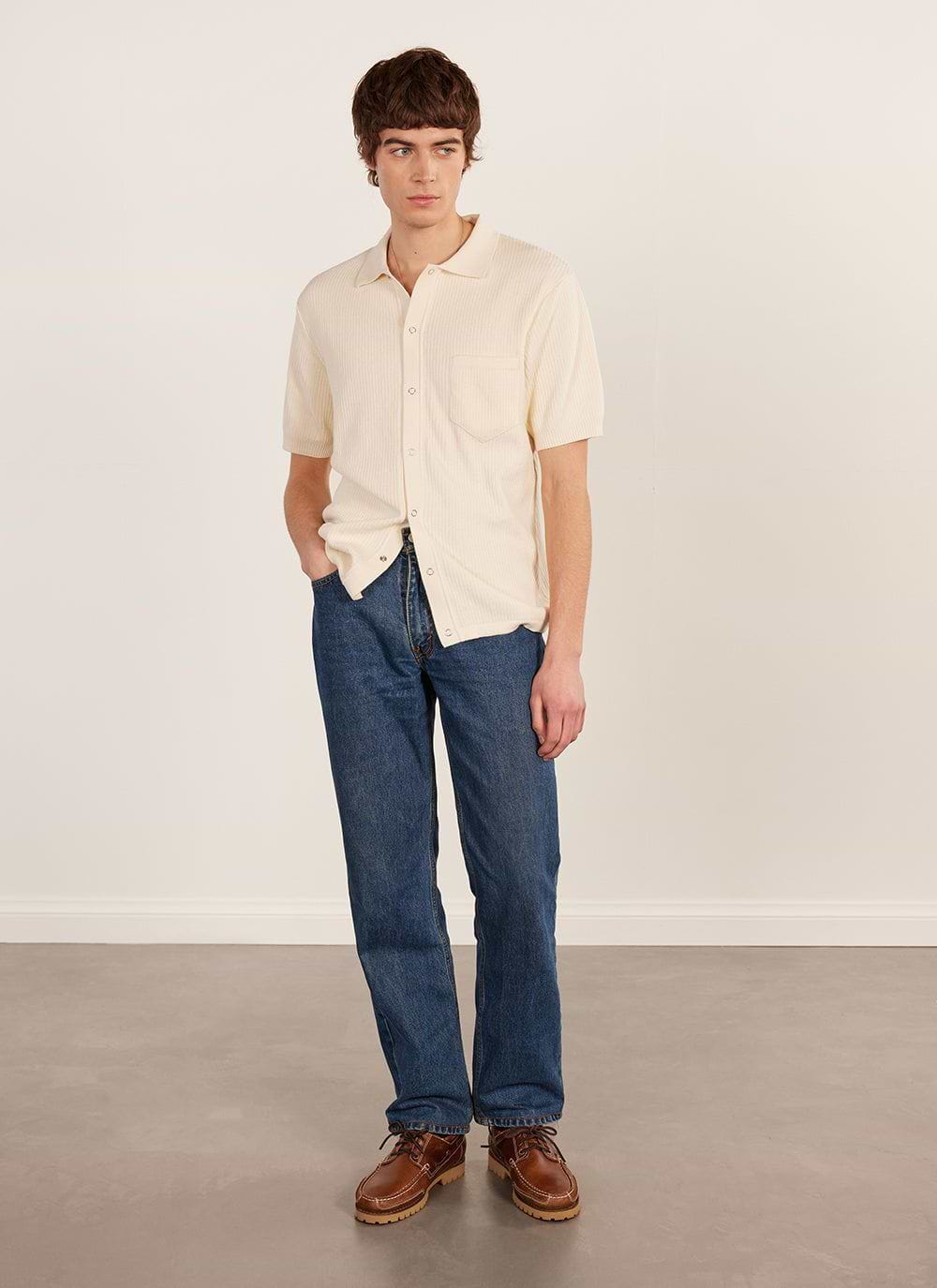 A model wears the Percival Pablo Cuban shirt in cream, a short-sleeved knitted style, with blue jeans and brown shoes.