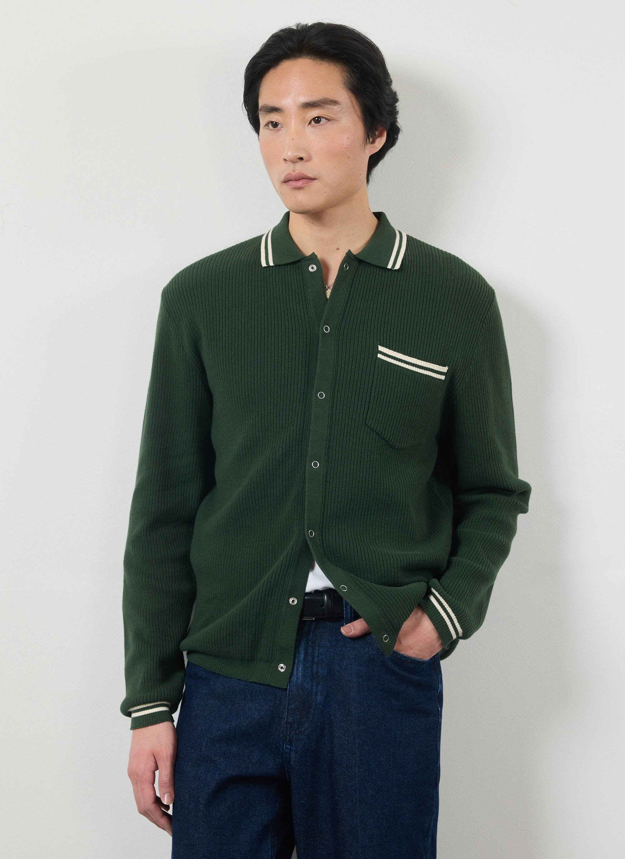 Model wears the Percival Pablo long sleeve knitted shirt in forest green with white stripes on the collar, pocket, and cuffs.