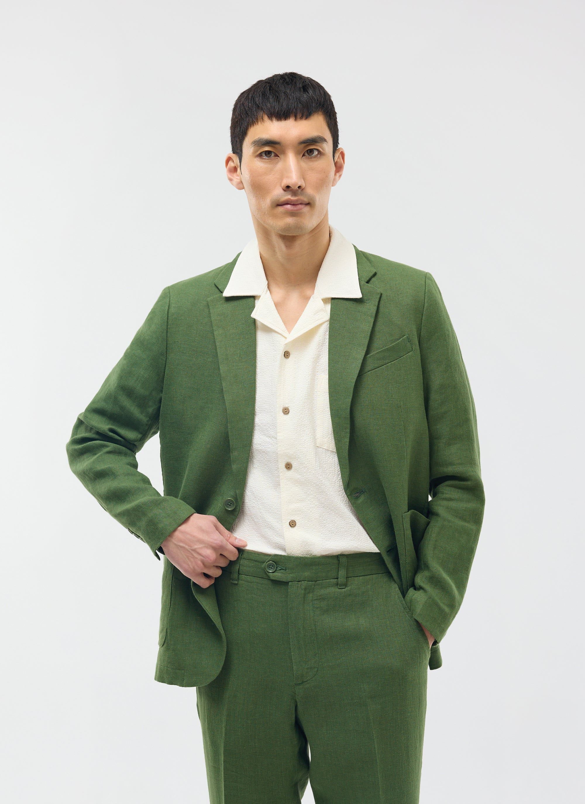 A model wears the Percival forest green linen blazer and matching trousers over a cream short-sleeved shirt.