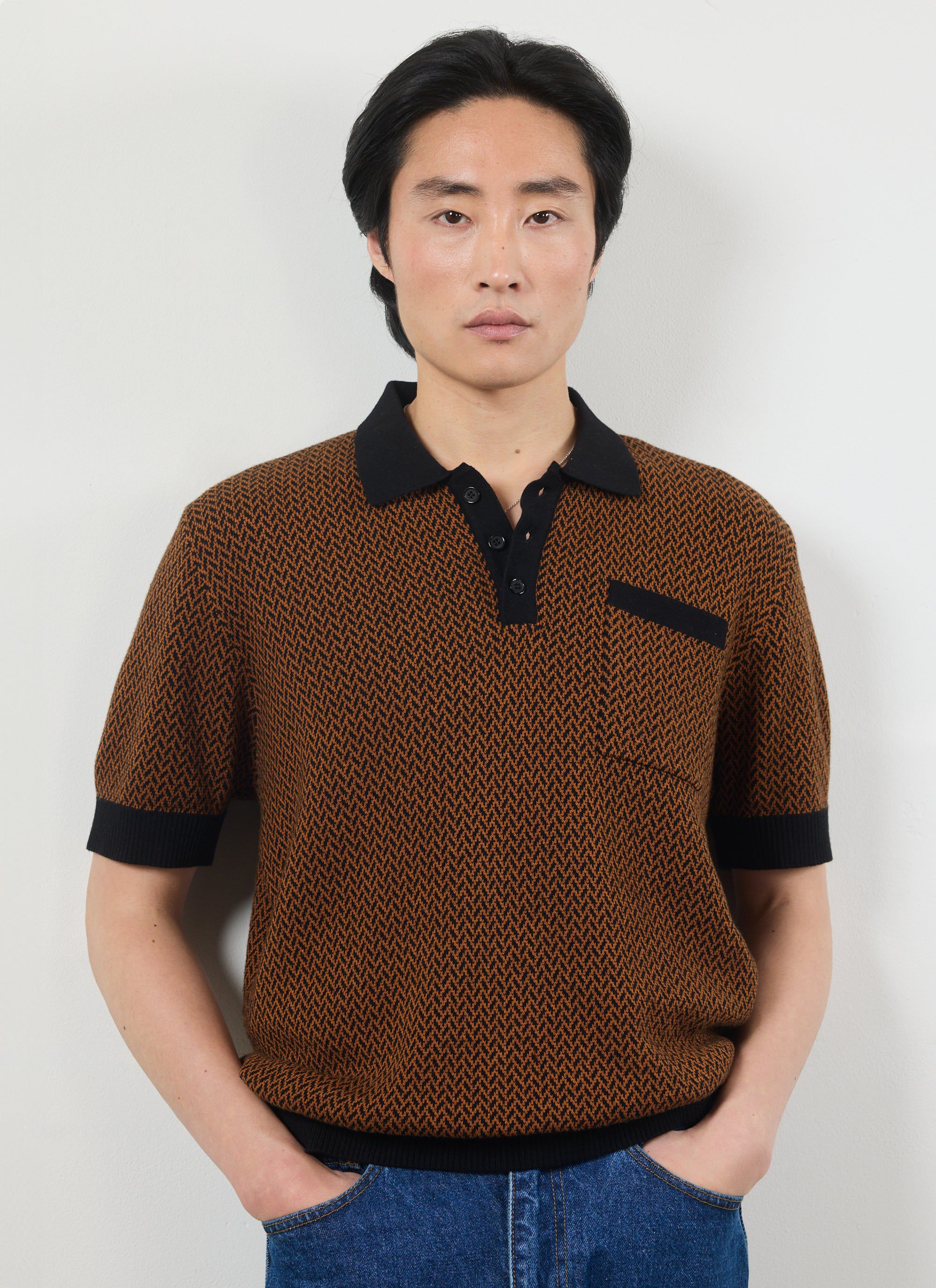 A model wears the Percival Casa Martini knitted polo shirt in espresso, a brown and black geometric knit with a black collar.
