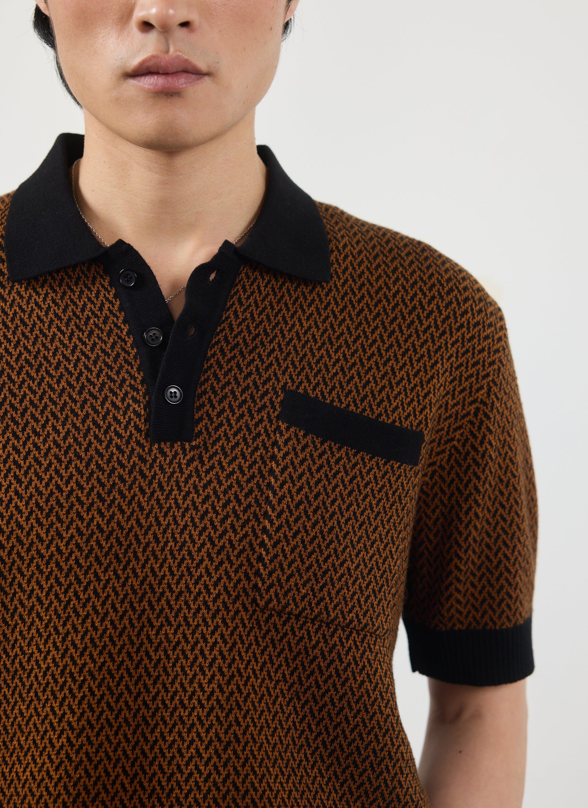 Close-up of a model wearing the Percival Casa Martini knitted polo shirt in an espresso brown and black zigzag pattern.