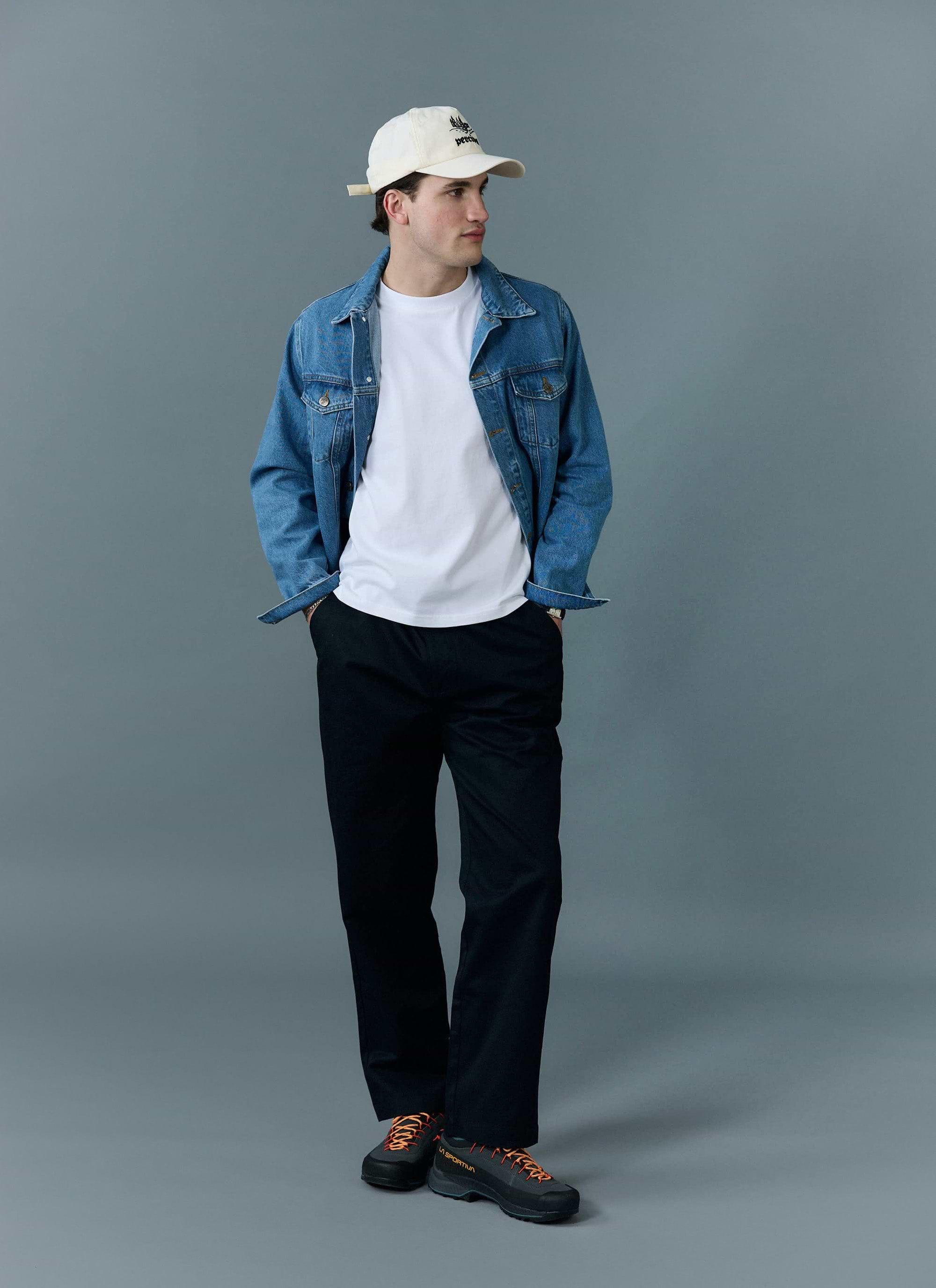A man models the Percival Western Trucker Jacket in light wash blue, styled over a white t-shirt with black trousers.