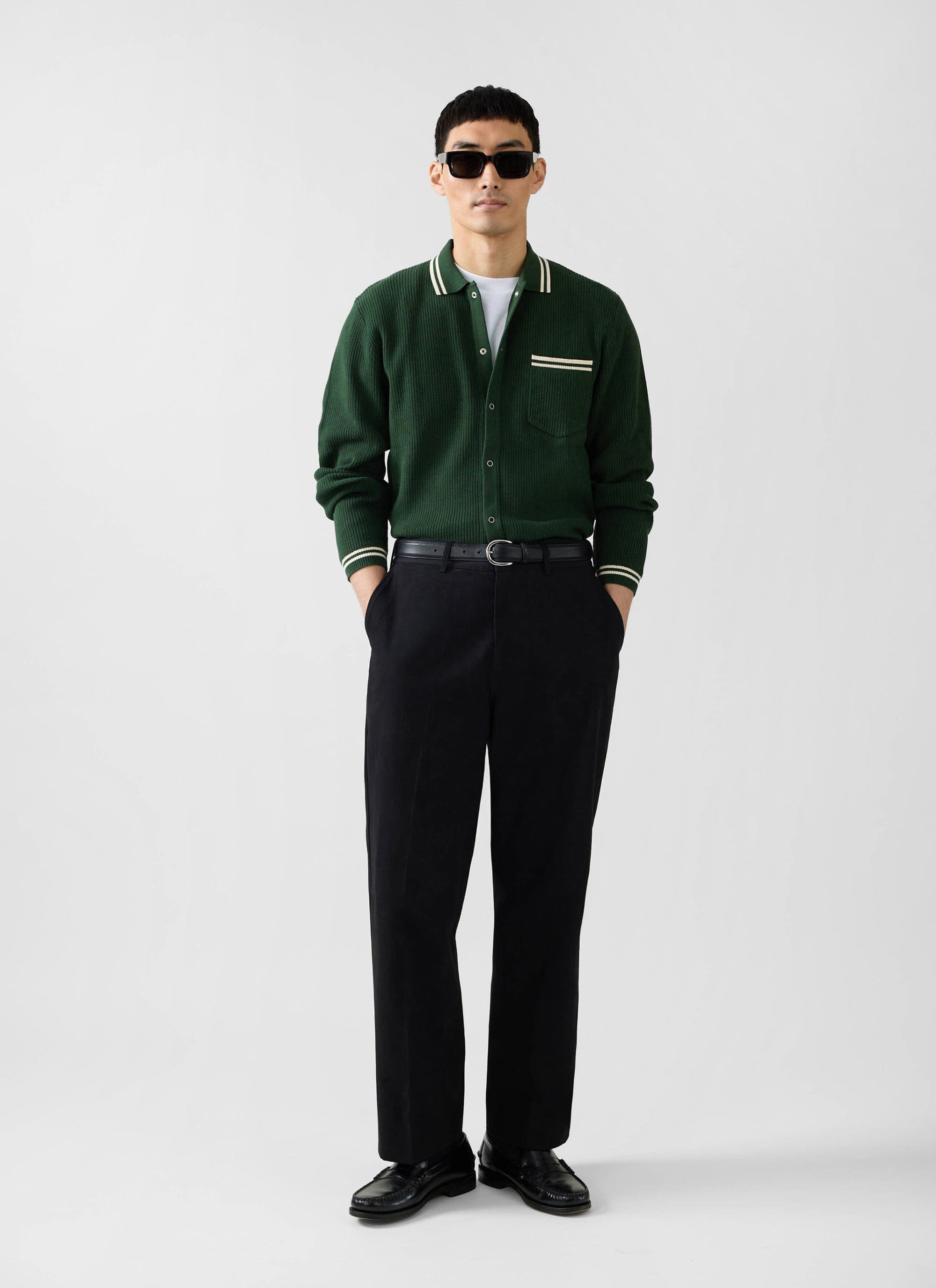 A model wears the Percival Pablo knitted shirt in forest green with black trousers and sunglasses against a white background.