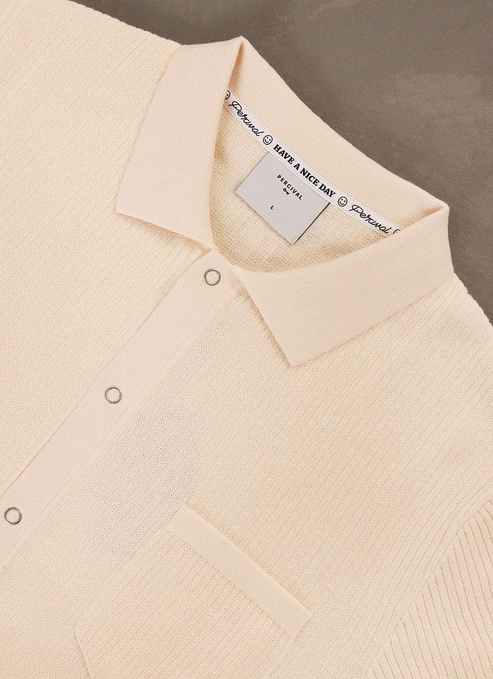 Close up of the Percival Pablo Cuban Shirt in cream, showing the knitted cotton fabric, collar and popper fastenings.