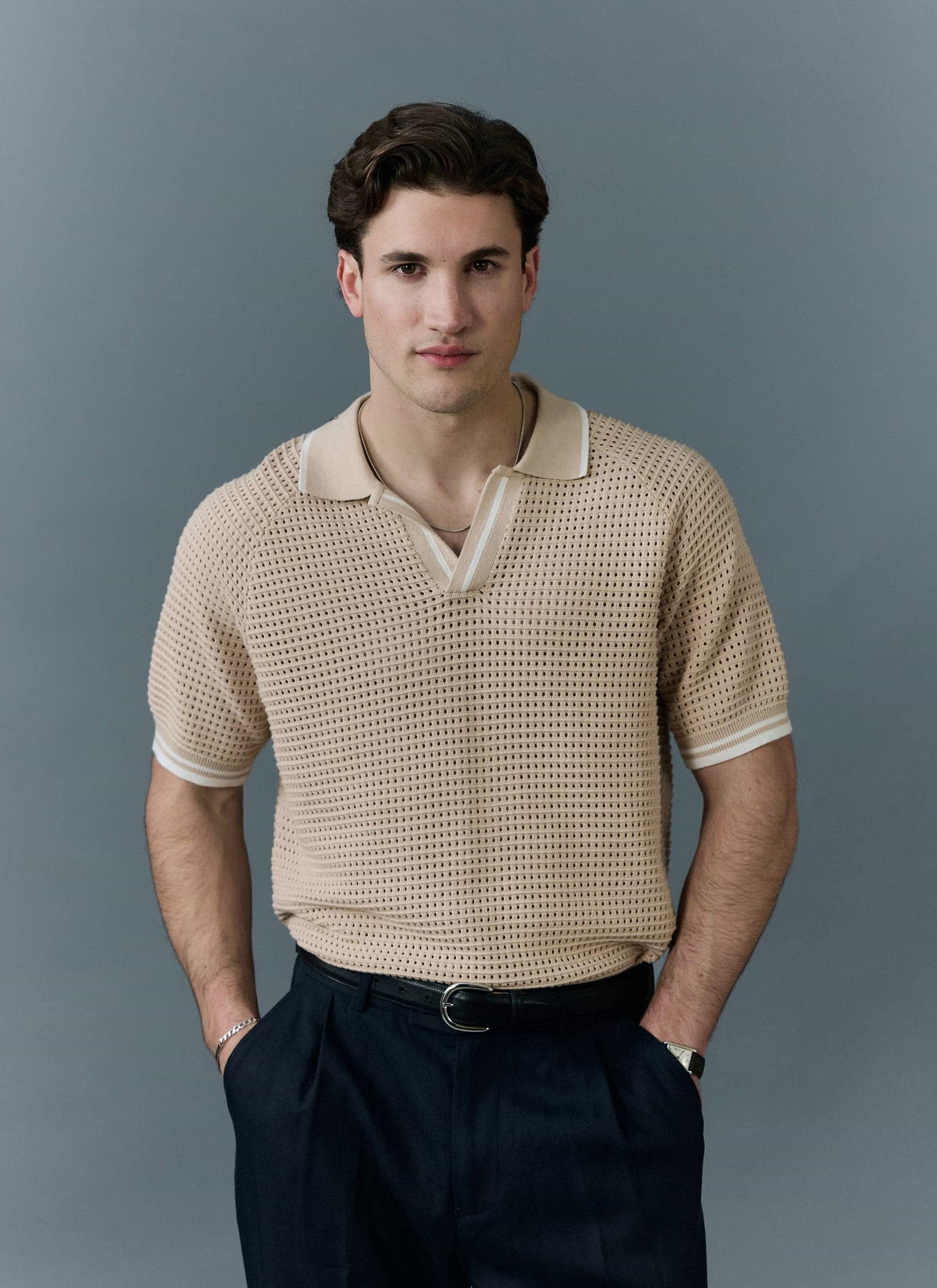 A model wears the Percival Tennis Boxy Knitted Polo in ecru, a cotton shirt with a perforated knit, on a grey background.
