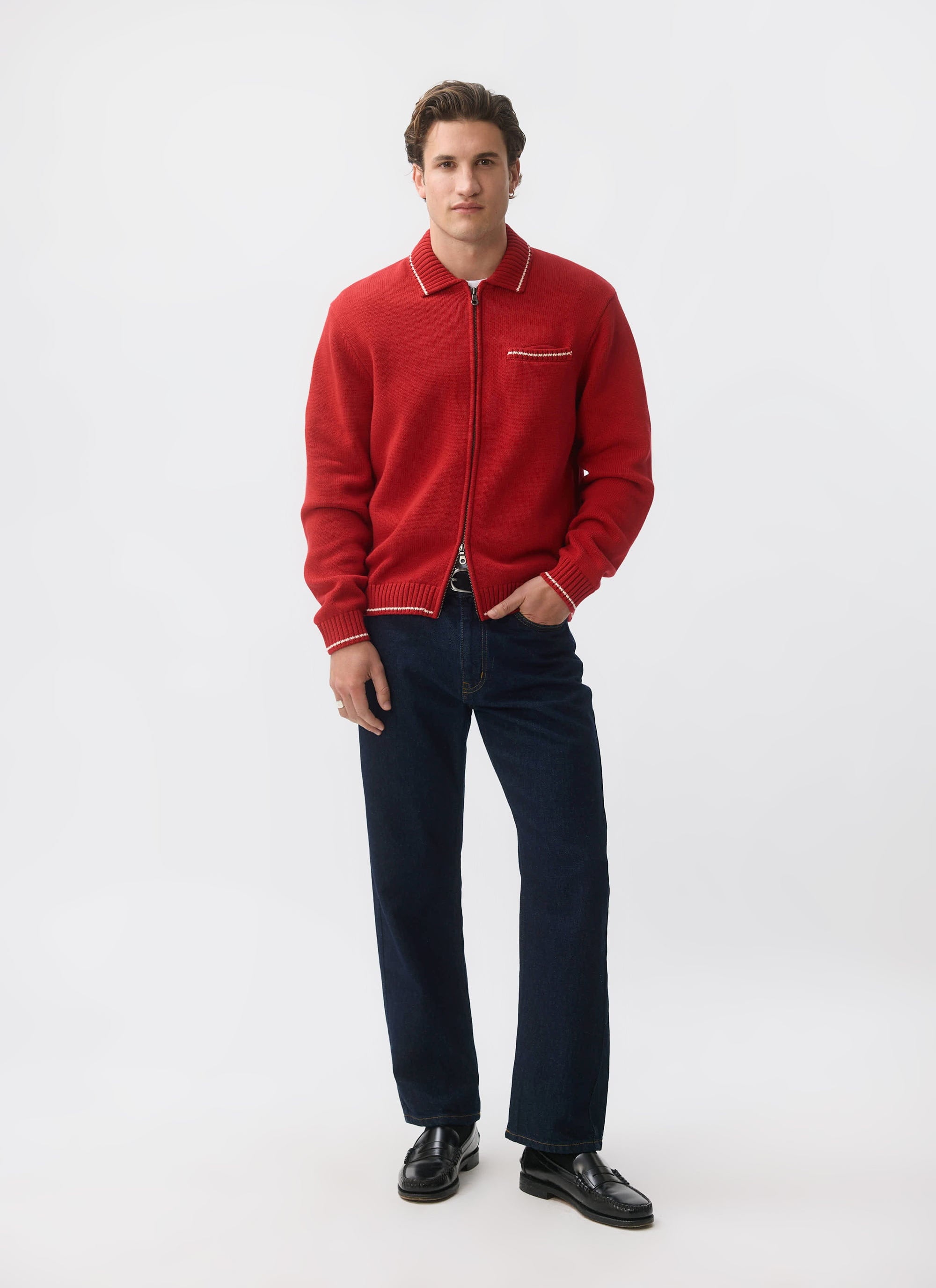 A man models the red Gardner Dense Knitted Zip Cardigan from Percival, styled with dark jeans and black loafers.