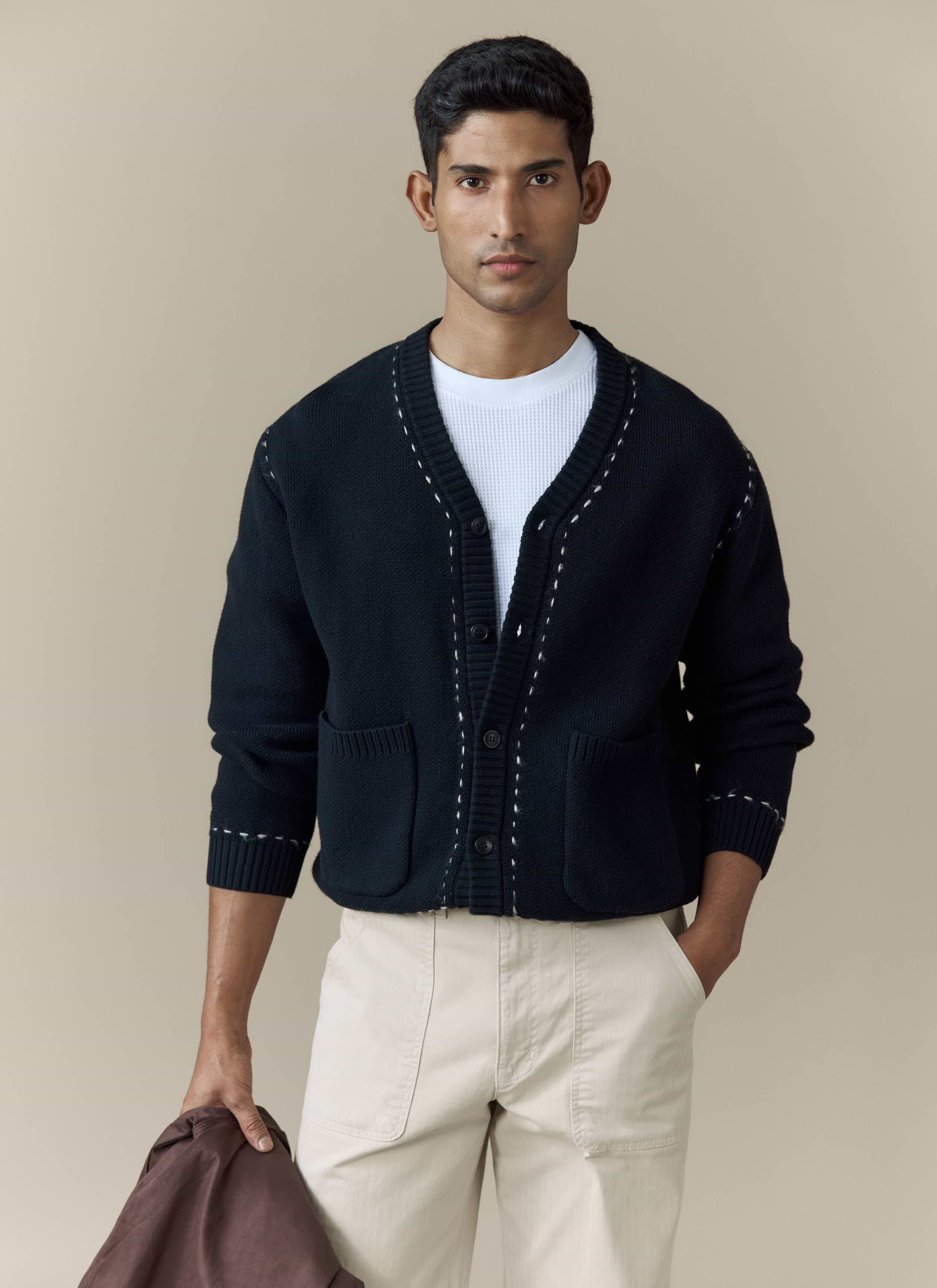 A model wears the black Module Boxy Cardigan from Percival, styled with a white t-shirt and cream trousers.
