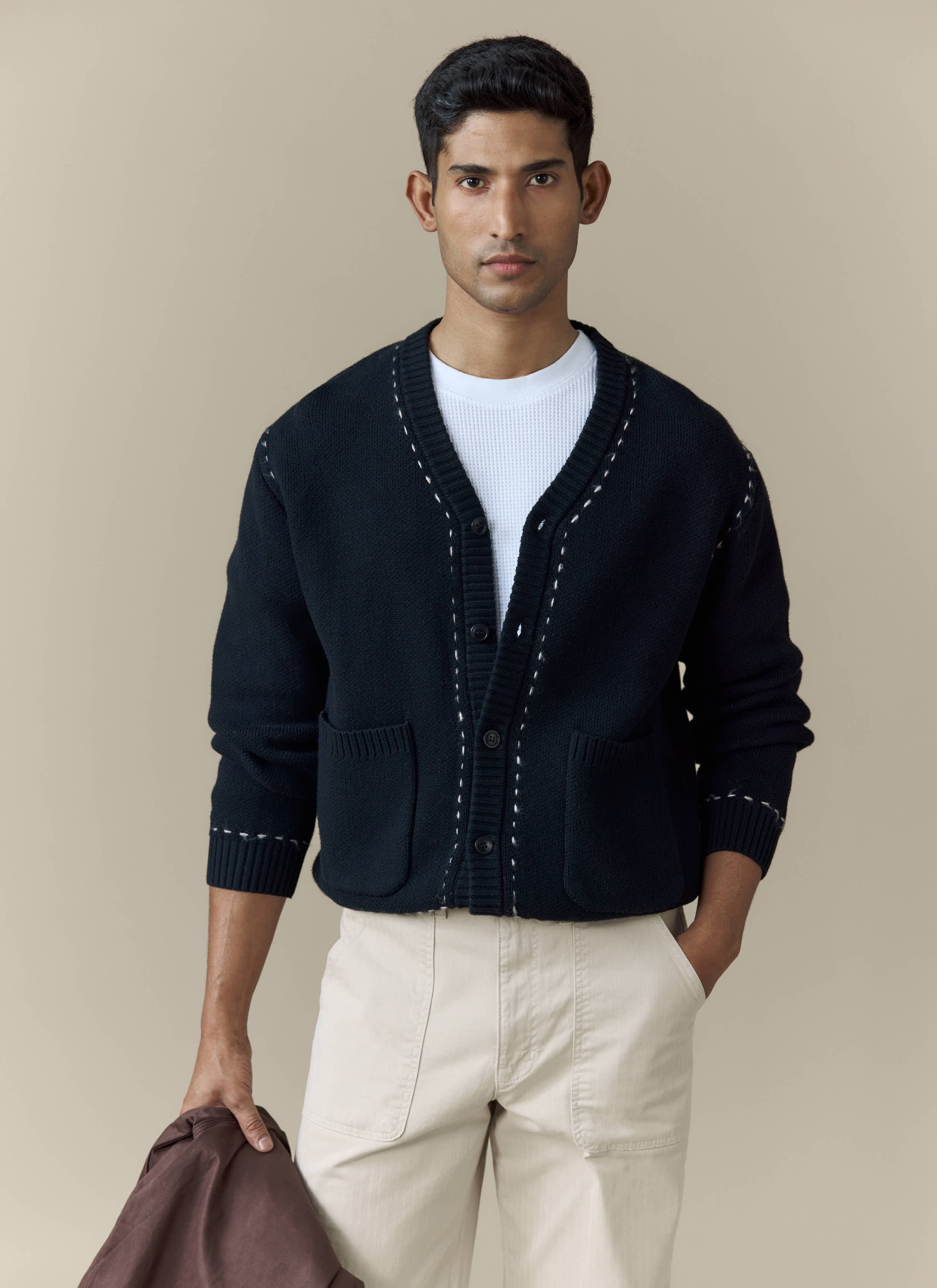 A model wears the black Module Boxy Cardigan from Percival, styled with a white t-shirt and cream trousers.