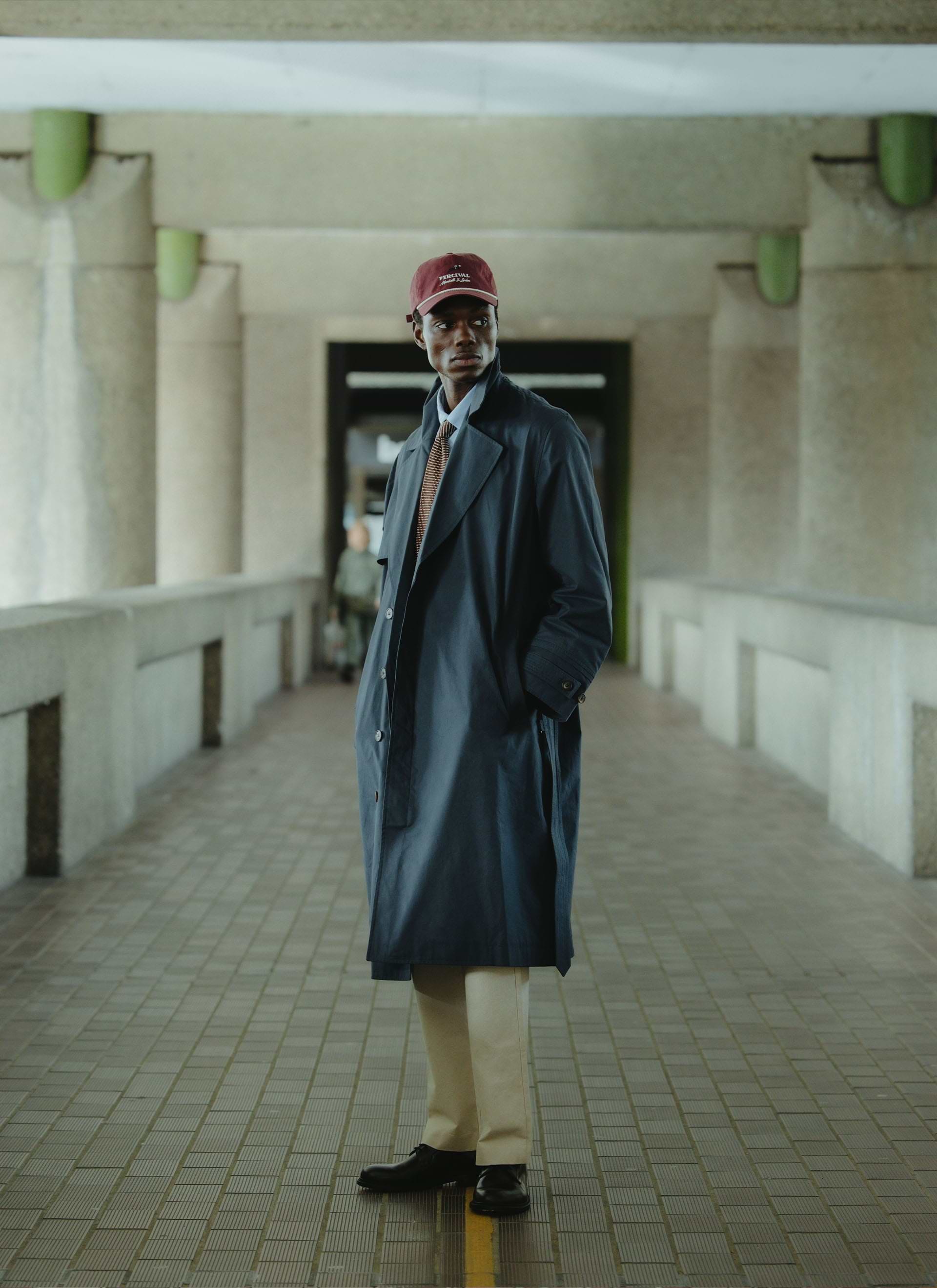 Navy Percival x Front Office Mac Trench Coat in peached cotton, styled with a burgundy cap in a concrete underpass.